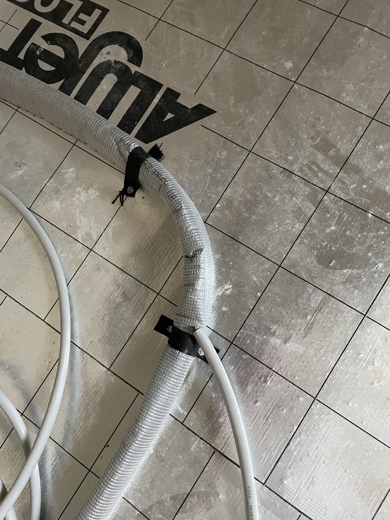 Silberne, flexible Metallkabel/Schlauch, gebogen, an Halterung auf staubigem Fliesenboden.