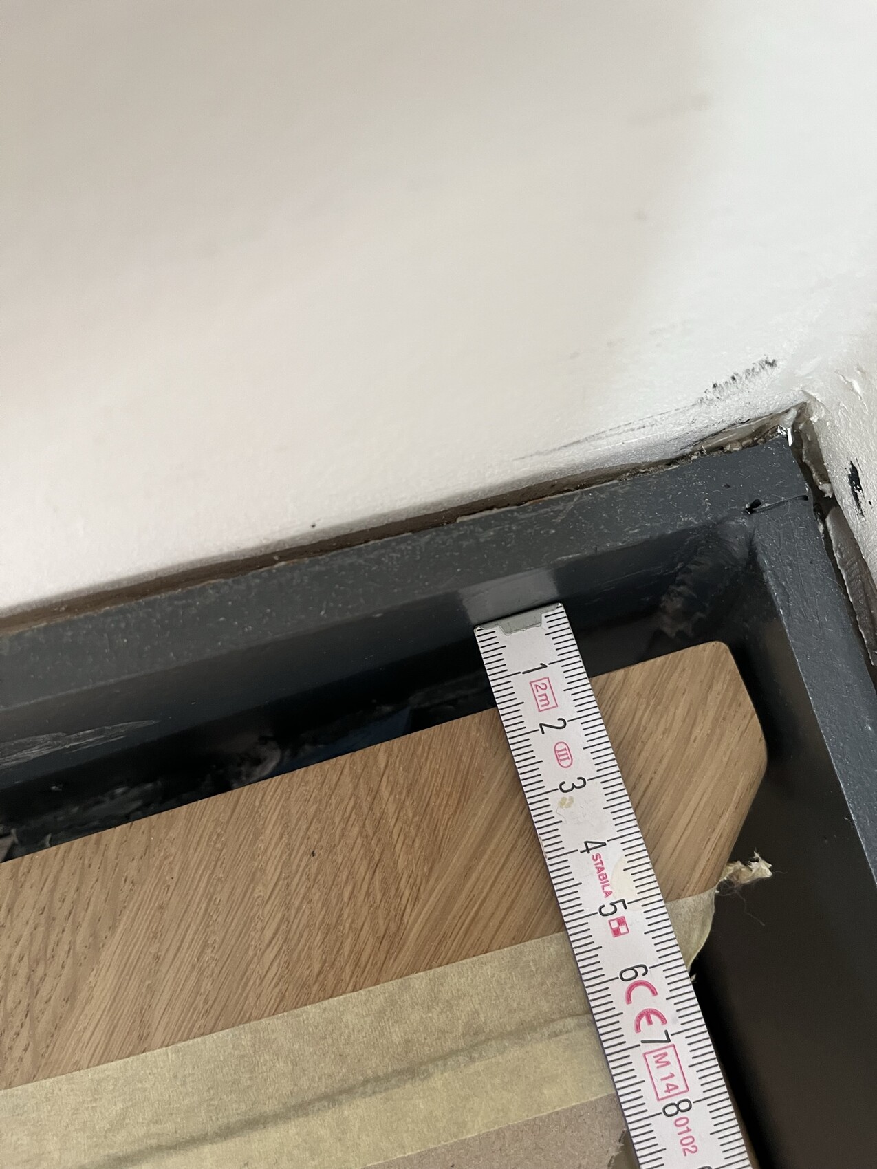 Nahaufnahme eines Türrahmens mit Maßband zur Vermessung, Holzfußboden sichtbar.