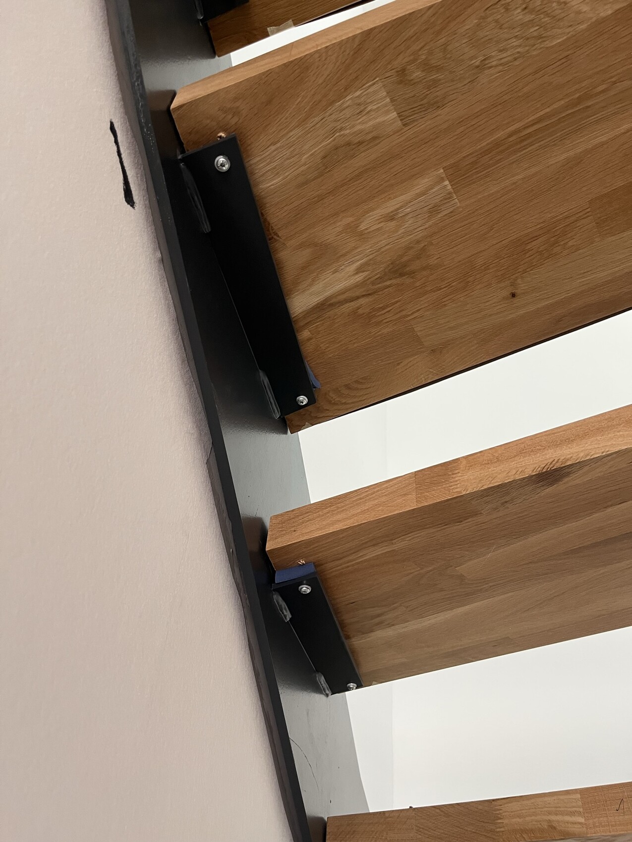 Holztreppenstufen mit schwarzen Metallhalterungen an einer Wand, Blick von unten.