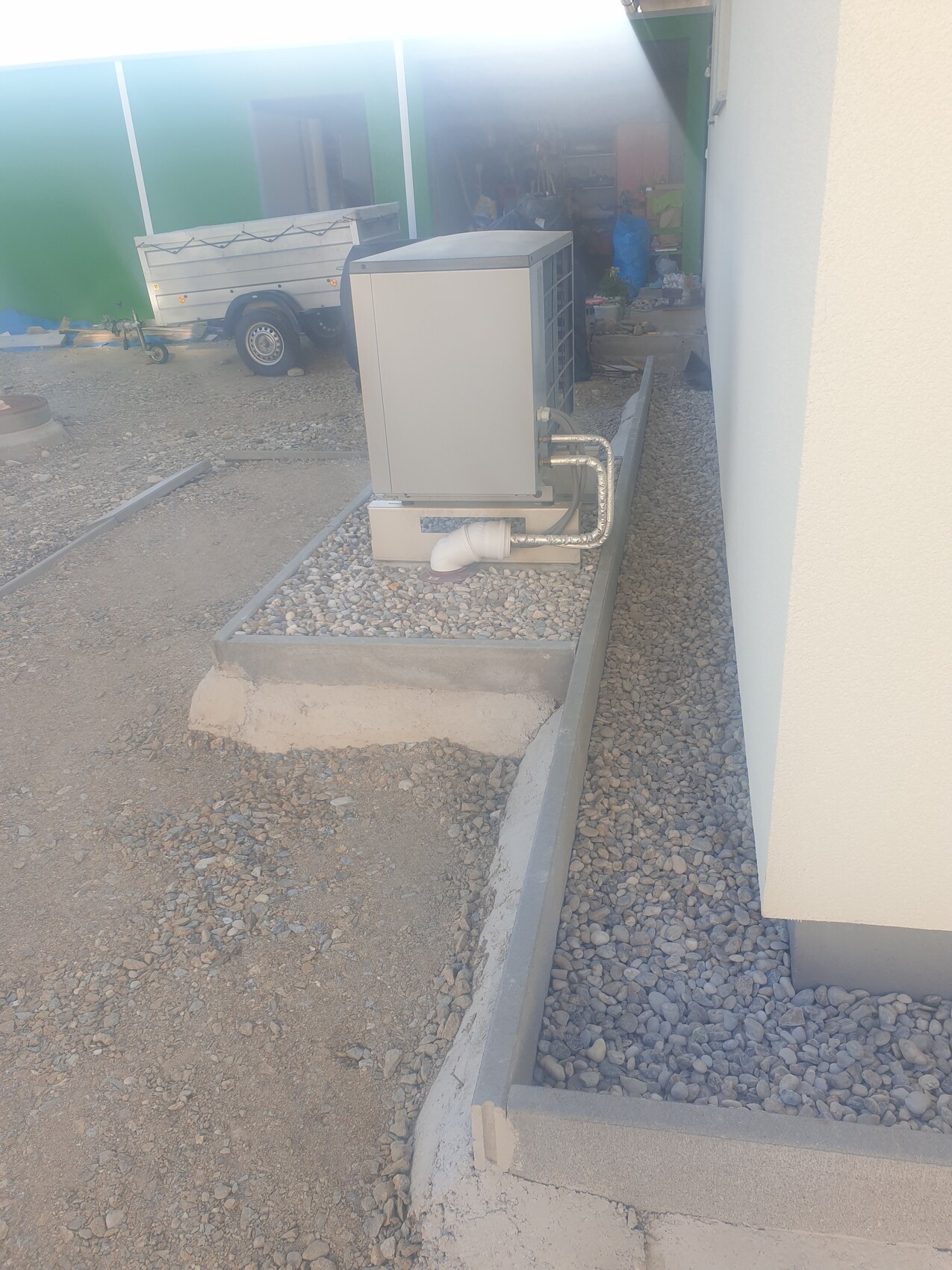 Klimagerätekondensator im Außenbereich auf Kies, Rohre führen zur Hauswand.