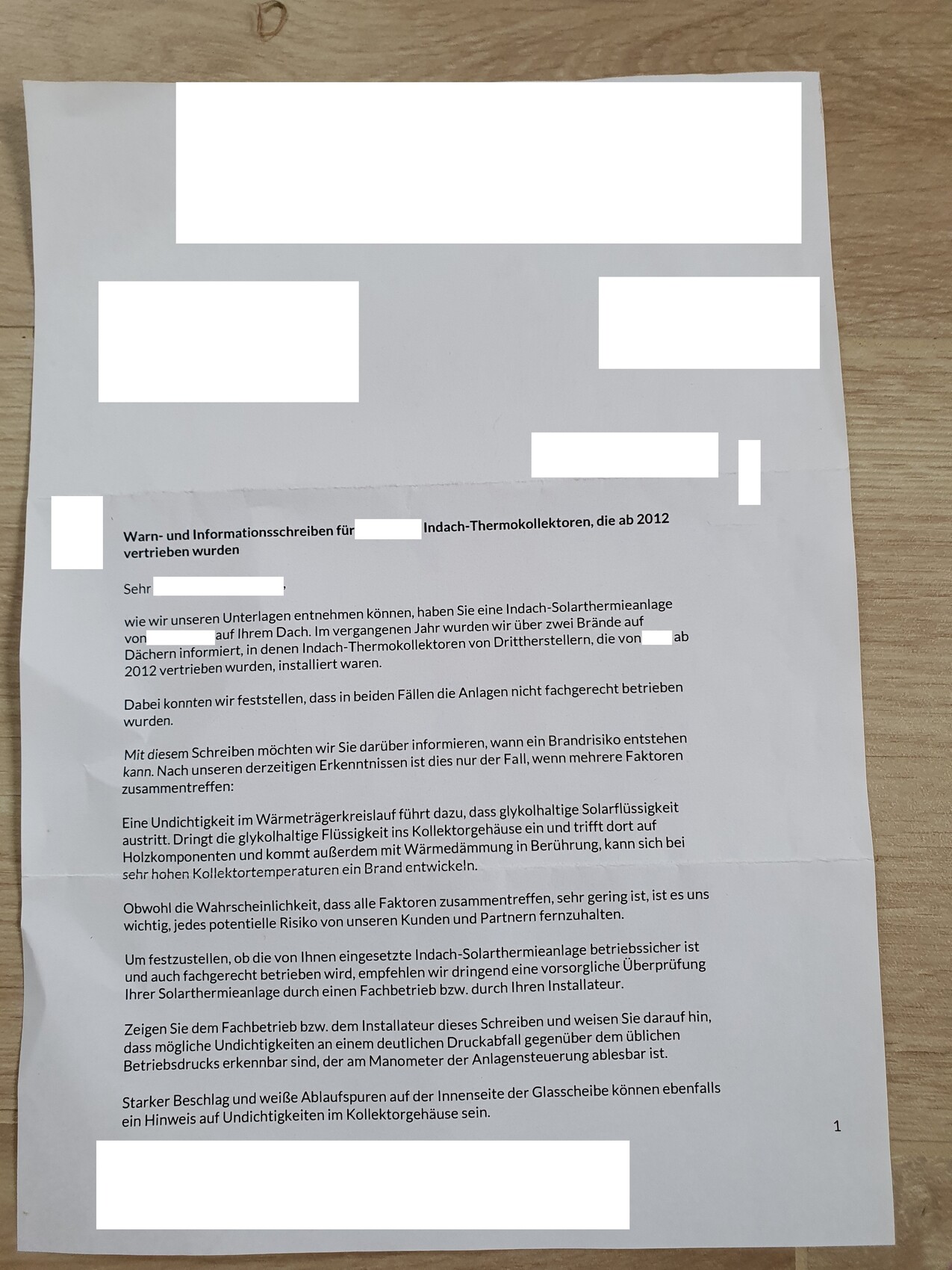 Ein Brief mit viel Text, teils abgedeckt durch weiße Rechtecke, liegt auf einem Holztisch.
