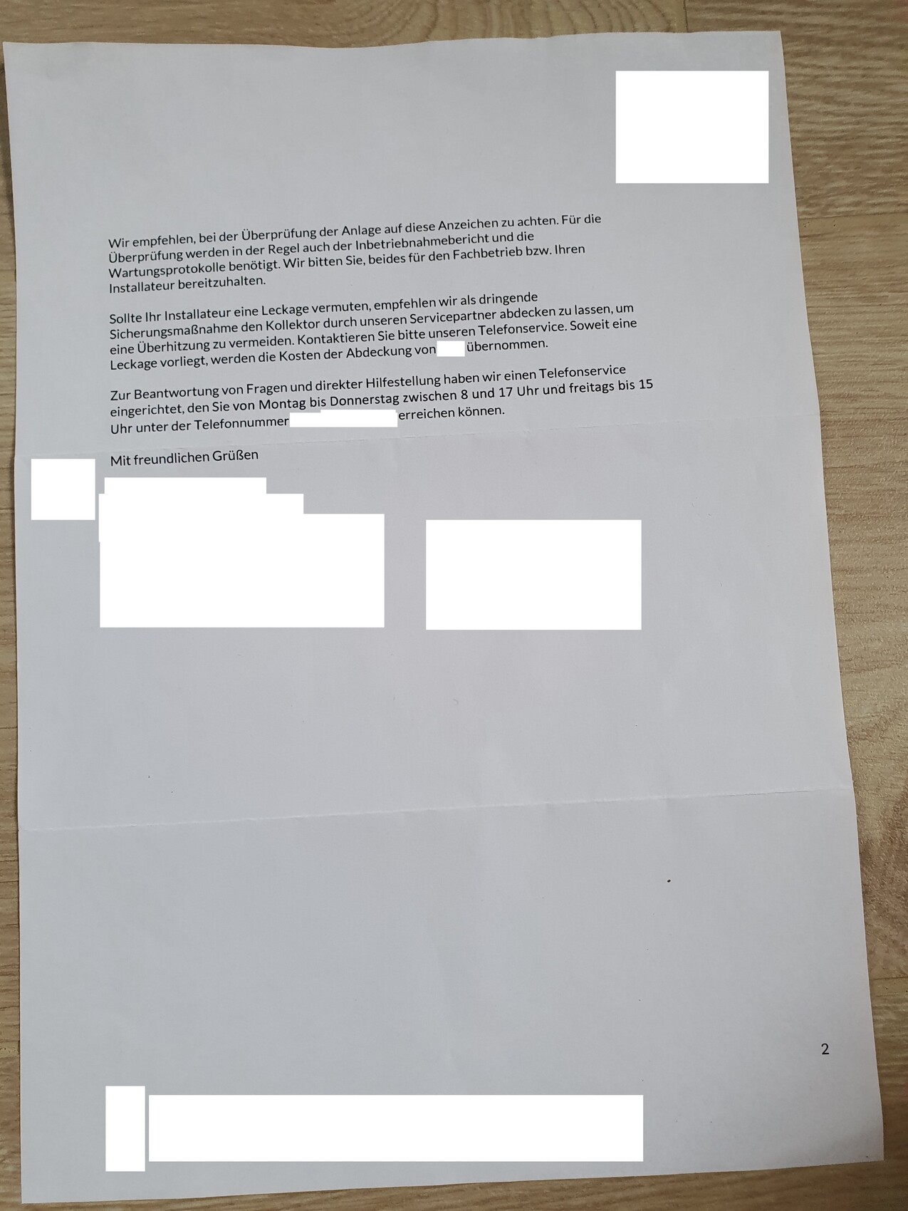 Ein Brief liegt auf einem Holztisch mit schwarzem Text und weißen Abdeckfeldern; Seite 2.