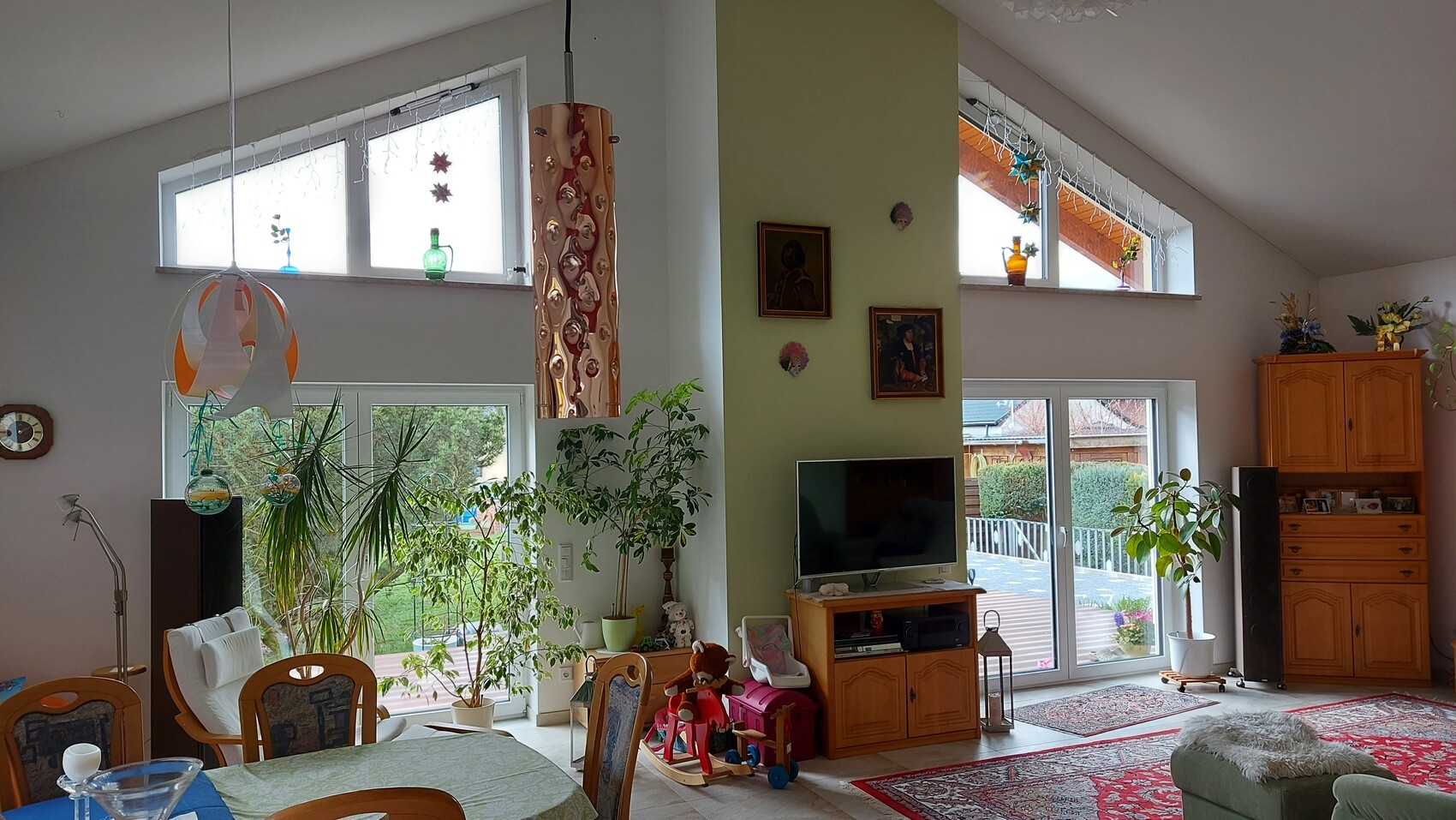 Helles Wohnzimmer mit vielen Topfpflanzen, TV auf Holzschrank, grüne Wand, Fenster zum Garten
