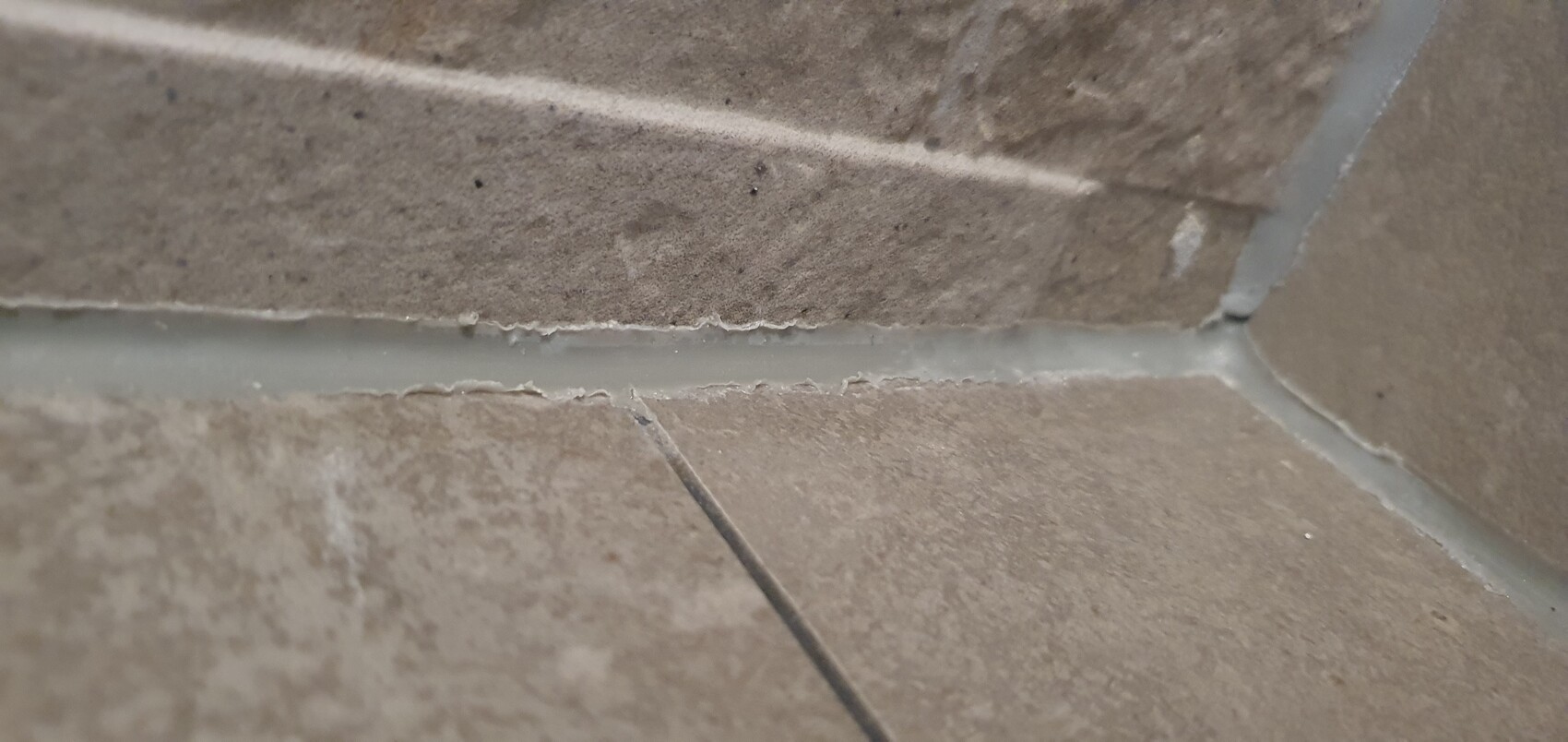 Nahaufnahme einer Fliesenfuge zwischen braunen Bodenfliesen mit grauer Fugenmasse