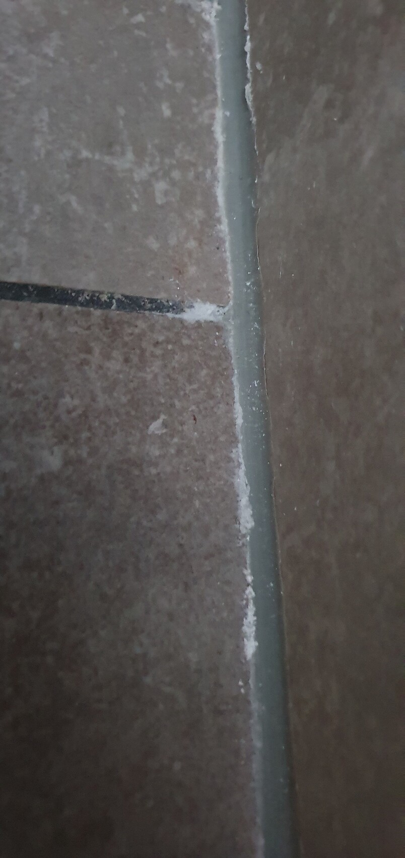 Nahaufnahme brauner Keramikfliesen mit grauer Fugenmörtel; weiße Kalkablagerungen an der Fuge.