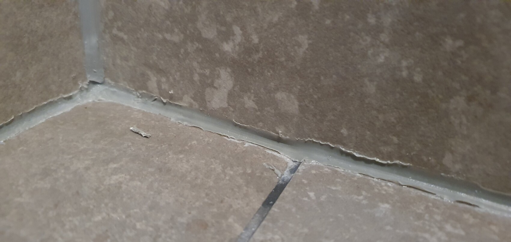 Eckbereich zweier brauner Bodenfliesen mit rissiger Fuge und abplatzenden Kanten.