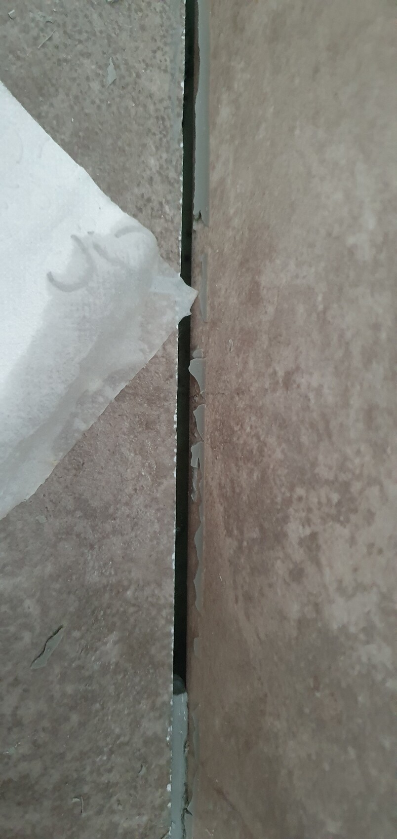 Enger Spalt zwischen zwei Bodenplatten; Fugenmasse blättert ab, Risse sichtbar.