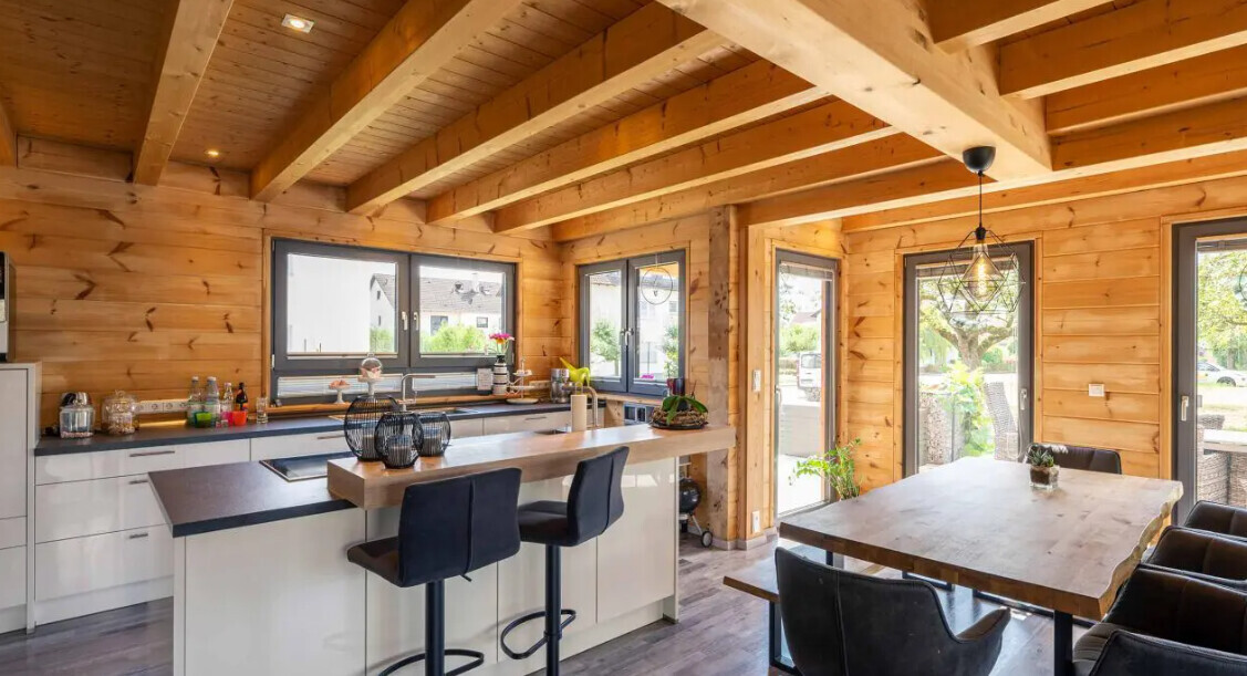 Moderne Küche in Holzhaus mit Insel, Barhockern, Esstisch und großen Fenstern.