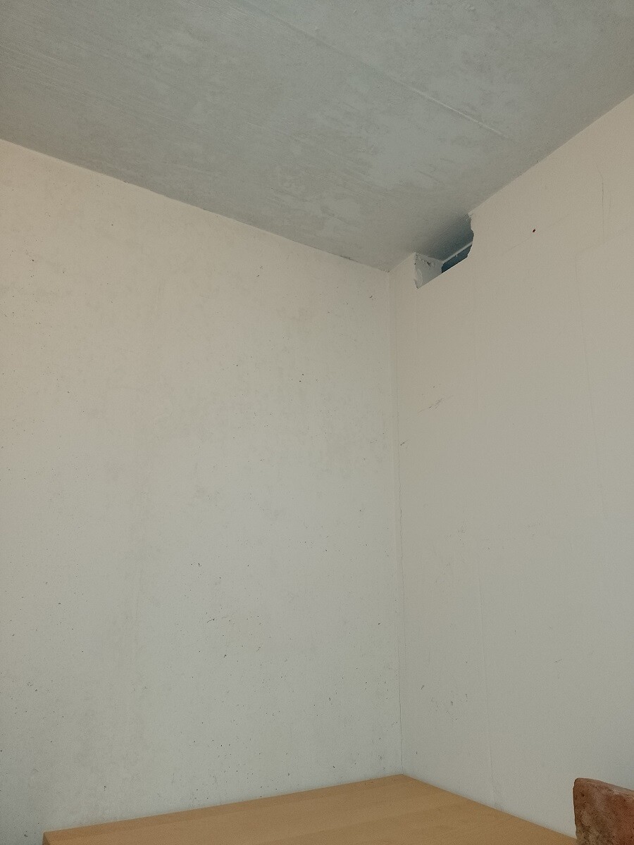 Leerer Raum mit weißen Wänden, grauer Decke, Ecke mit Öffnung und Holztisch im Vordergrund.