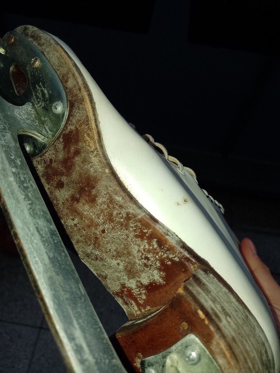 Nahaufnahme eines rostigen Eiskunstlauf-Skates mit weißem Schuh und Metallklinge.