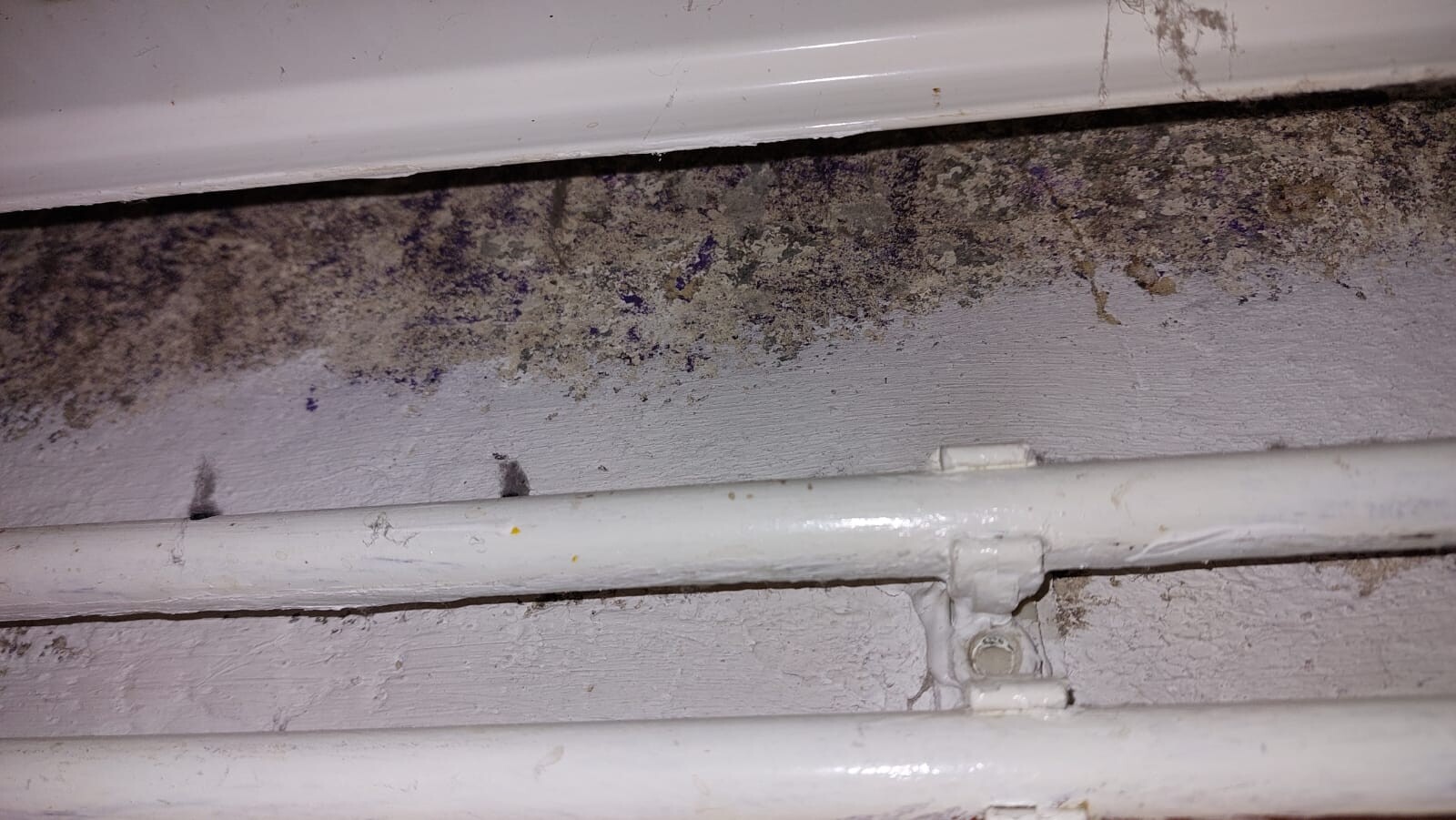 Nahaufnahme von zwei weißen Rohren entlang einer schmutzigen Wand mit Schimmel- und Rostflecken.