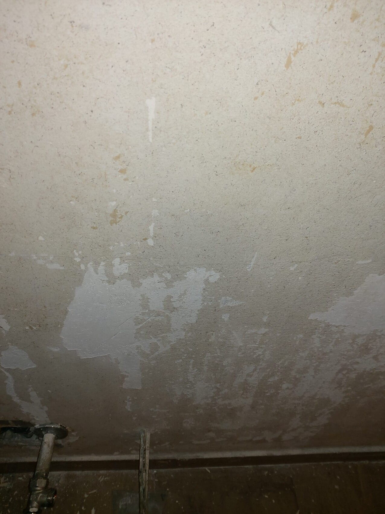 Feuchte Kellerwand mit abblätternder Farbe und sichtbaren Rohren am Boden.