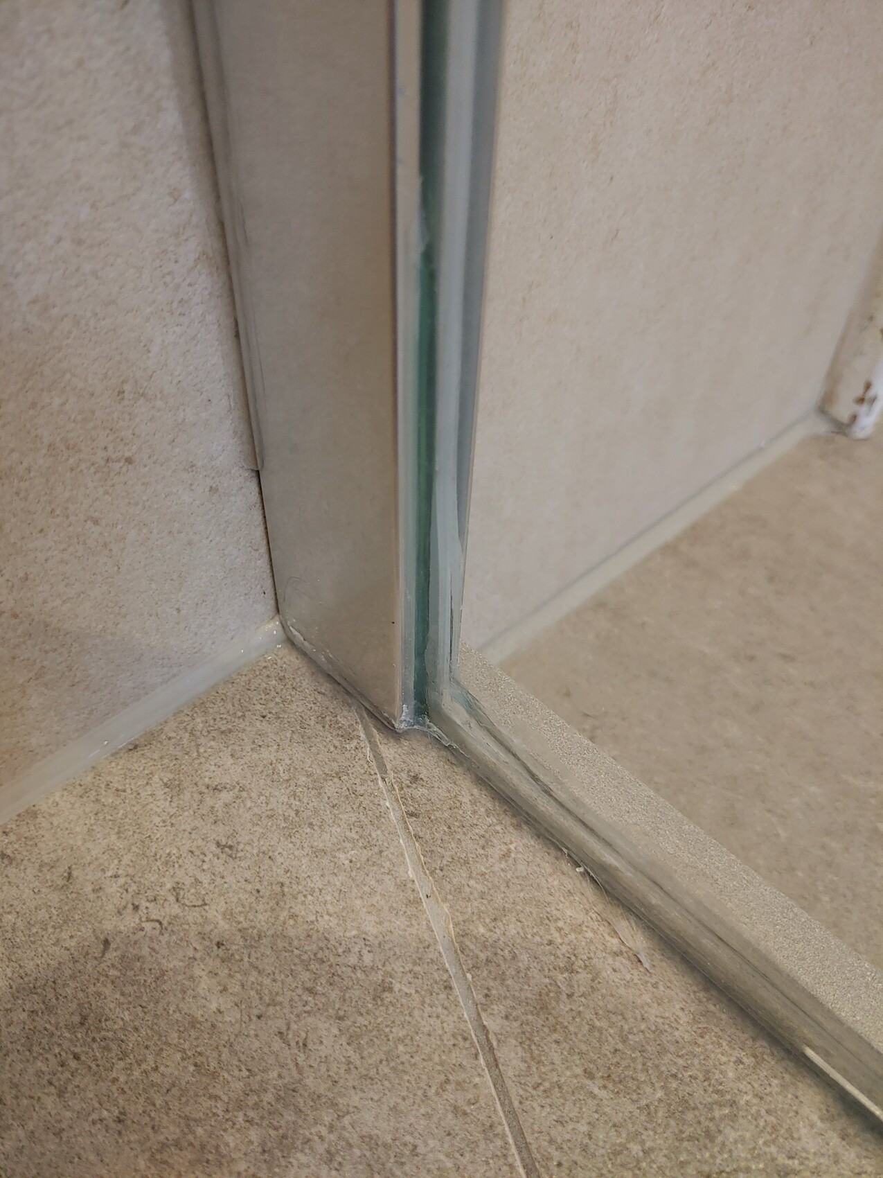 Nahaufnahme einer Türschwelle aus Metall am Boden, Fliesen und Dichtungen sichtbar.