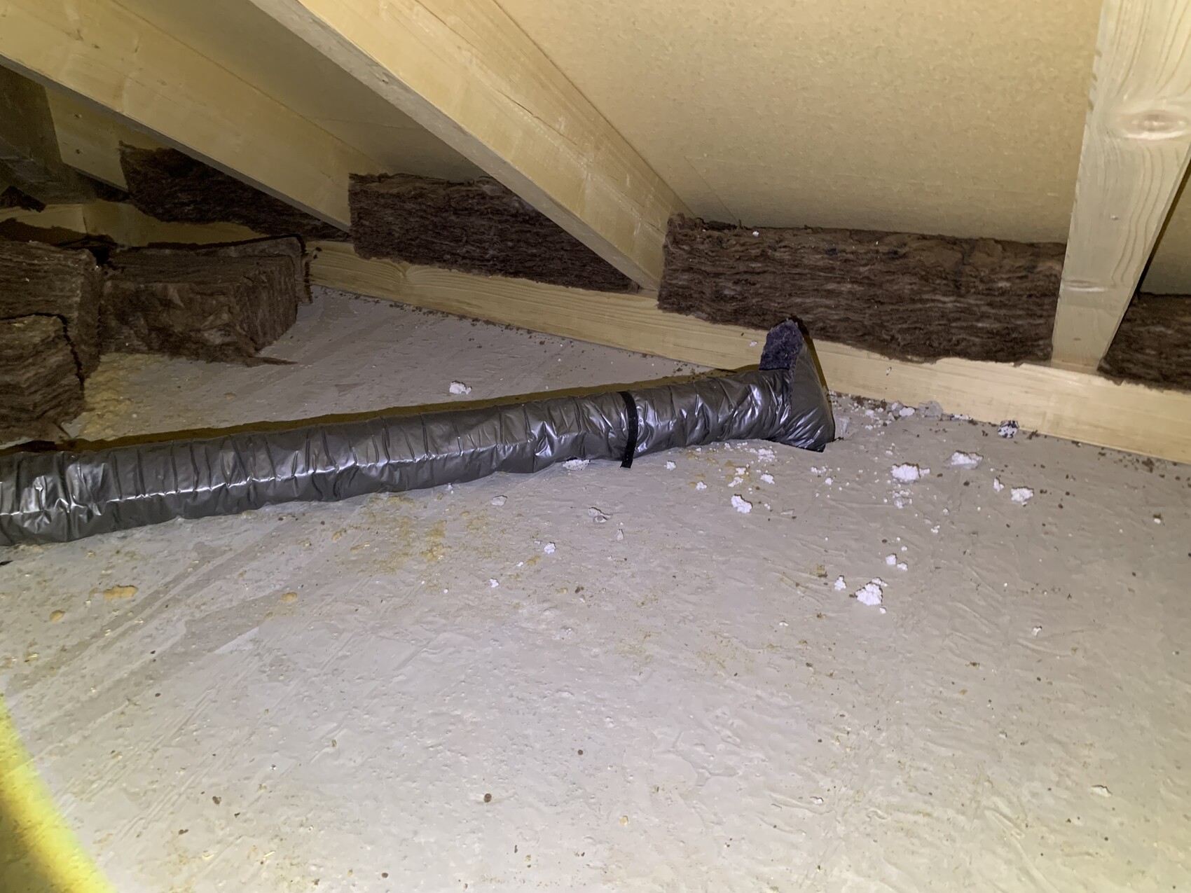 Dachboden: langer, flexibler silberner Lüftungsschlauch auf Betonboden neben Dämmmaterial.