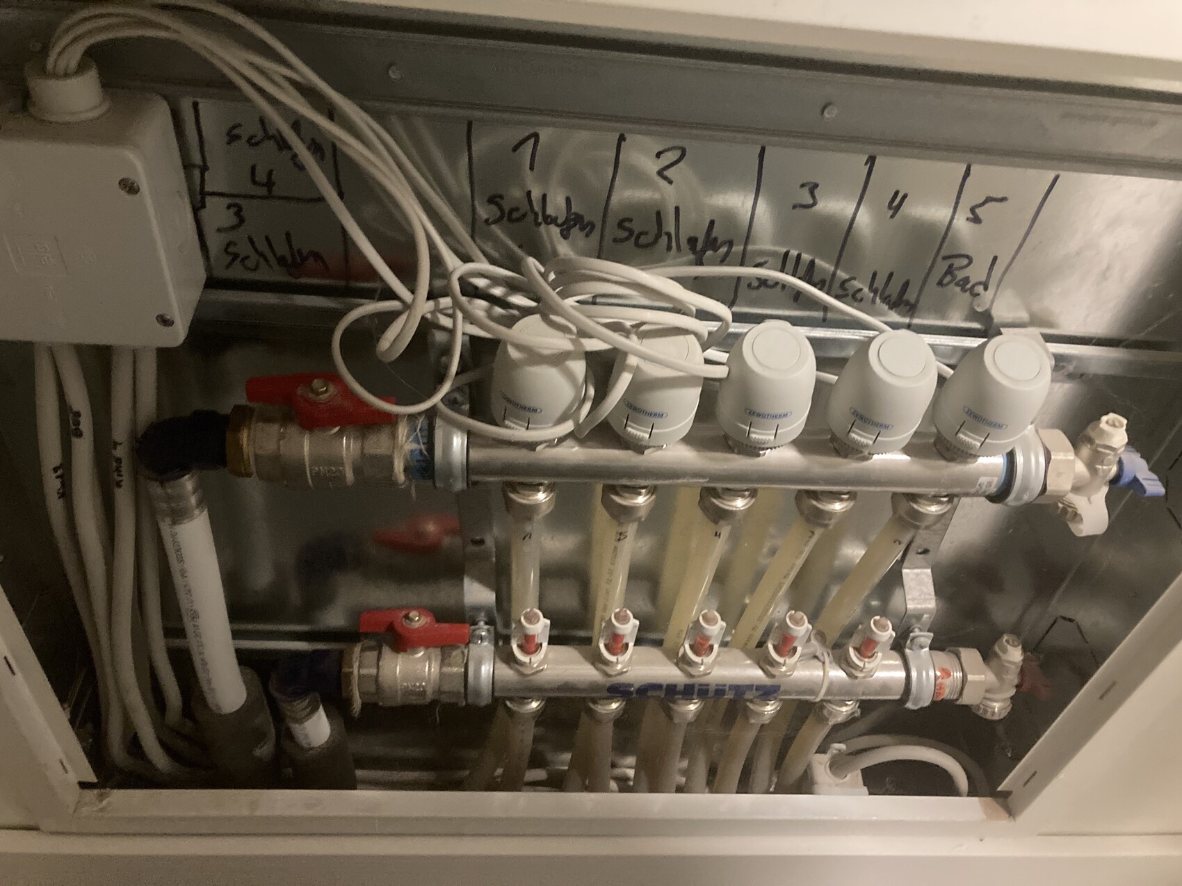 Heizungsverteiler mit Thermostatventilen, Rohren und Metallrahmen.