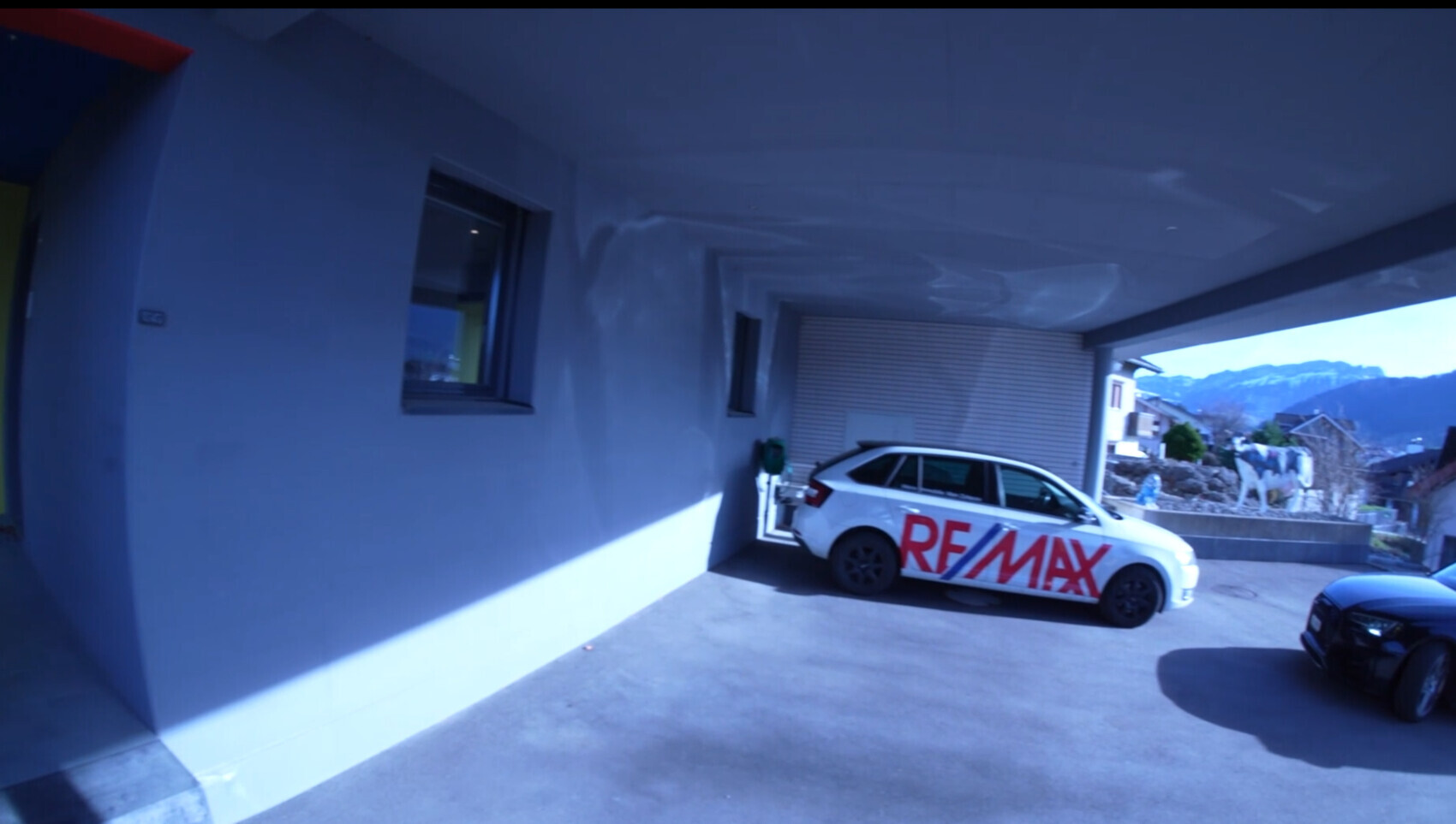 Weisser RE/MAX Wagen parkt im Carport unter Ueberdachung, Berge im Hintergrund