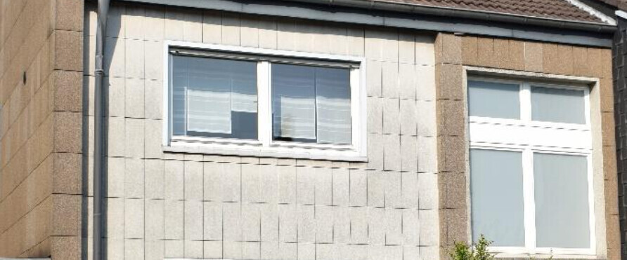 Fassade eines Wohnhauses mit zwei weißen Fenstern und grauen Fassadenplatten