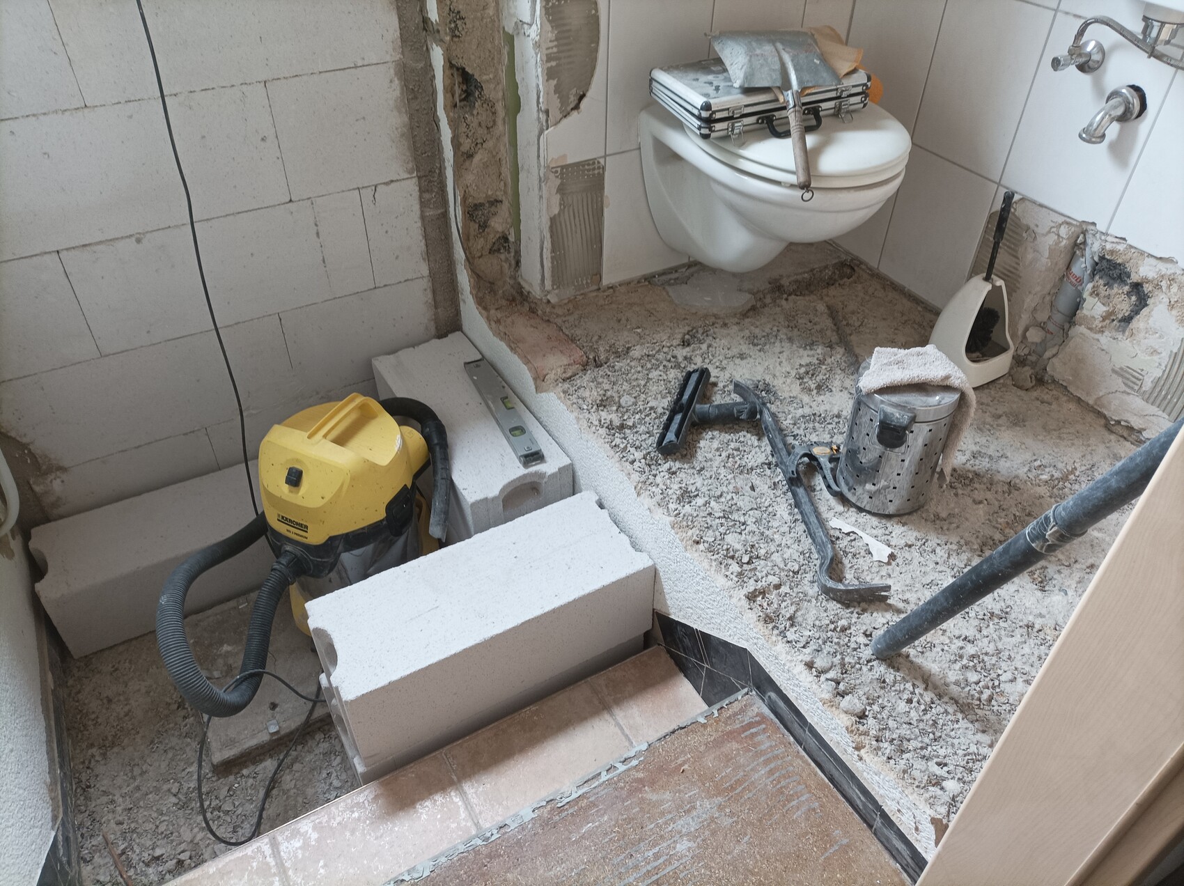 Badezimmer im Umbau: freigelegte Wand, provisorisch installierte Toilette, Baustoffreste.