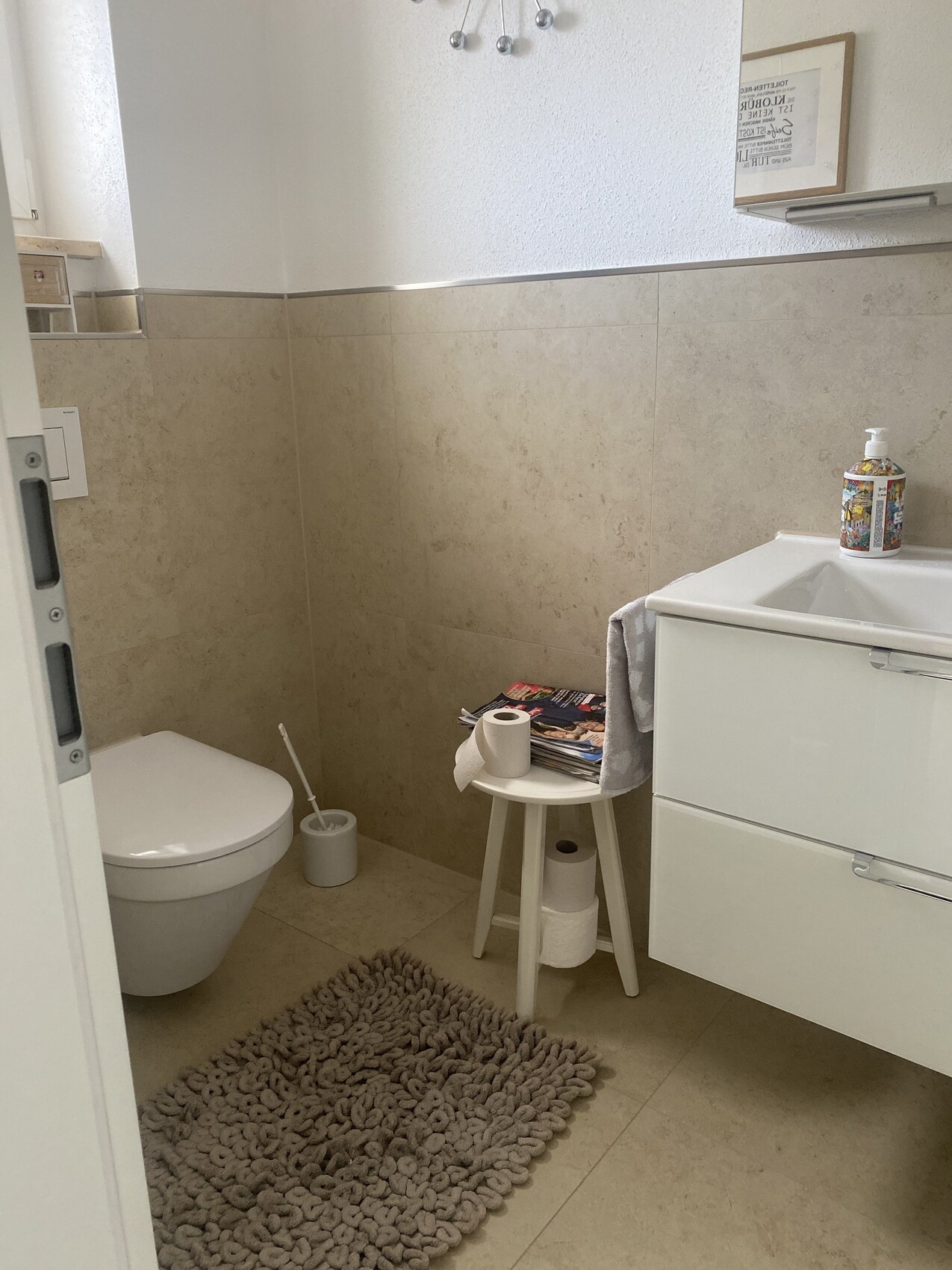 Helles Badezimmer mit Toilette, Waschbecken, Unterschrank und grauem Badteppich