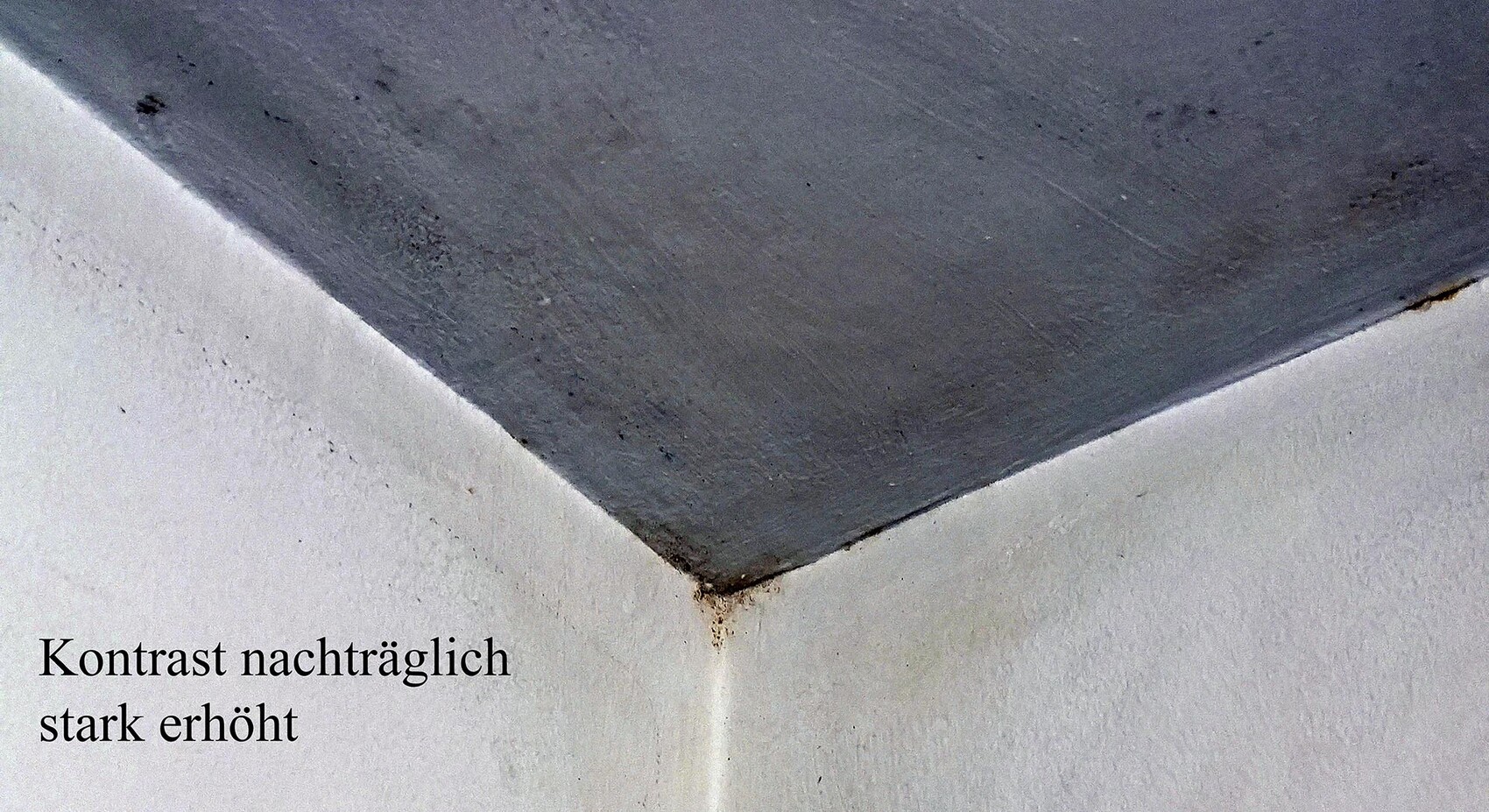 Winkel zwischen weißer Wand und dunkelgrauer Decke, rostige Flecken an der Ecke sichtbar.