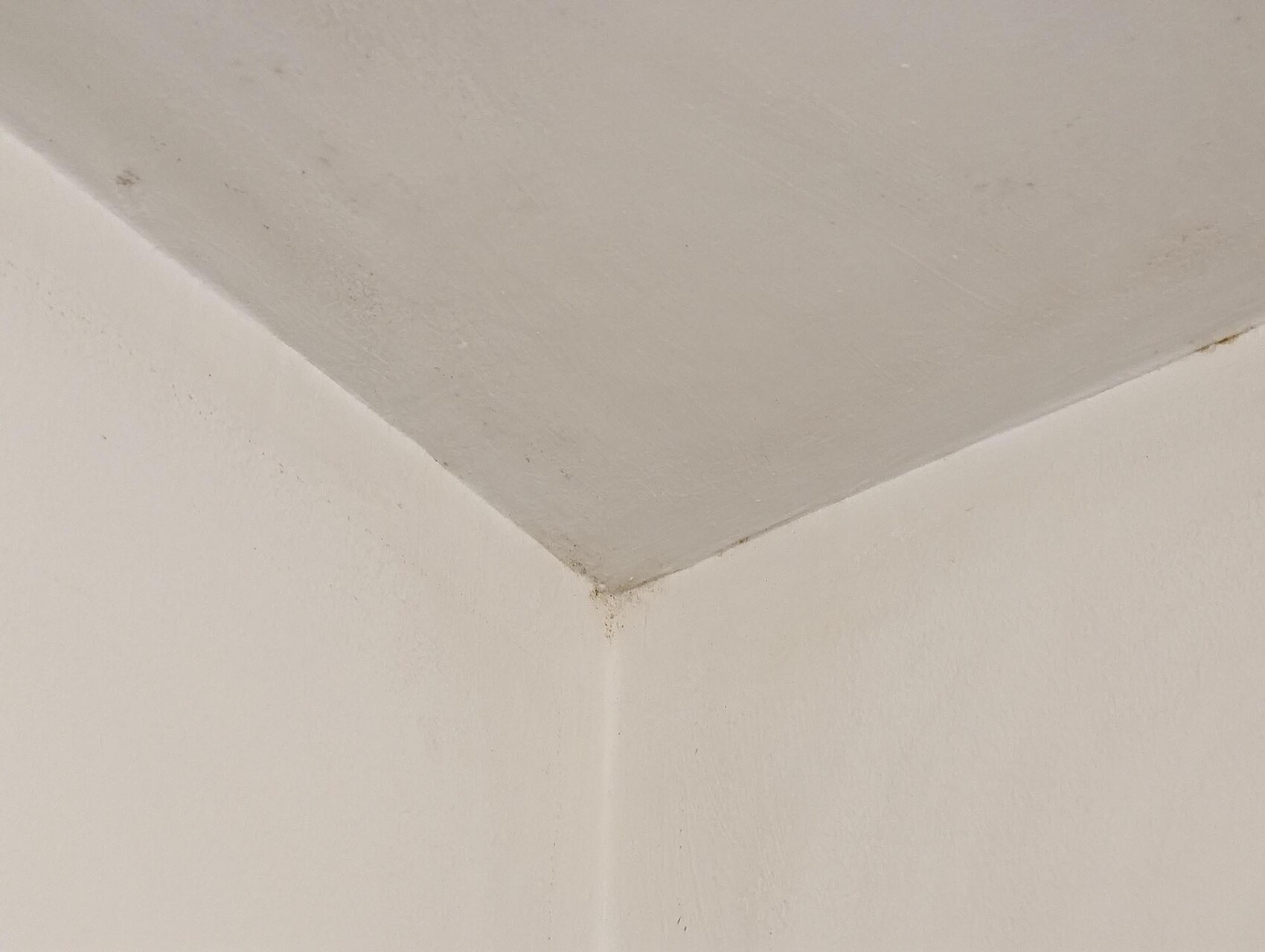 Weiße Innenraumecke: zwei Wände treffen sich, schräge Deckenkante, Verschmutzung an der Ecke.