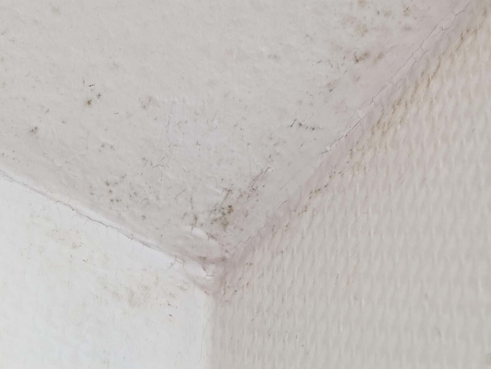 Nahaufnahme einer weißen Wand mit diagonalen Rissen, Flecken und unregelmäßiger Oberfläche.