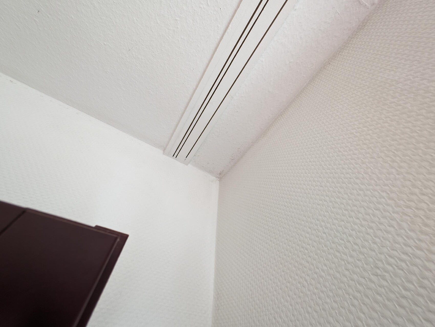 Winkel eines weißen, texturierten Innenraums mit dunklem Möbelstück unten links.