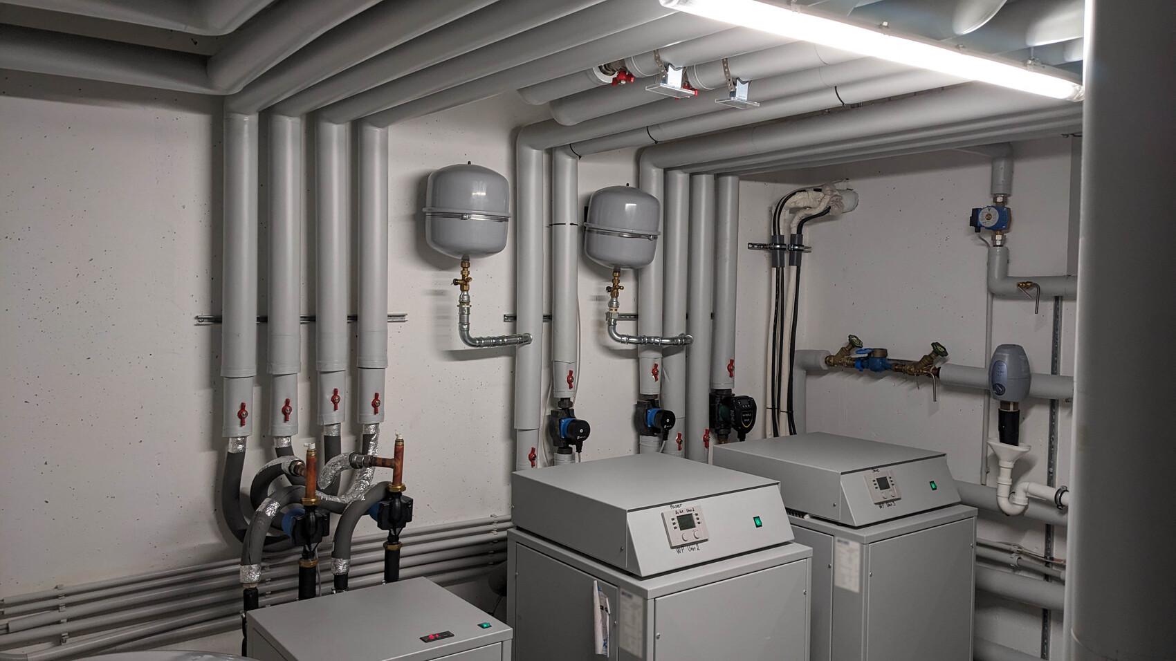 Kellerraum: Heizungsanlage mit isolierten Rohren, zwei Expansionsbehälter und Pumpen.