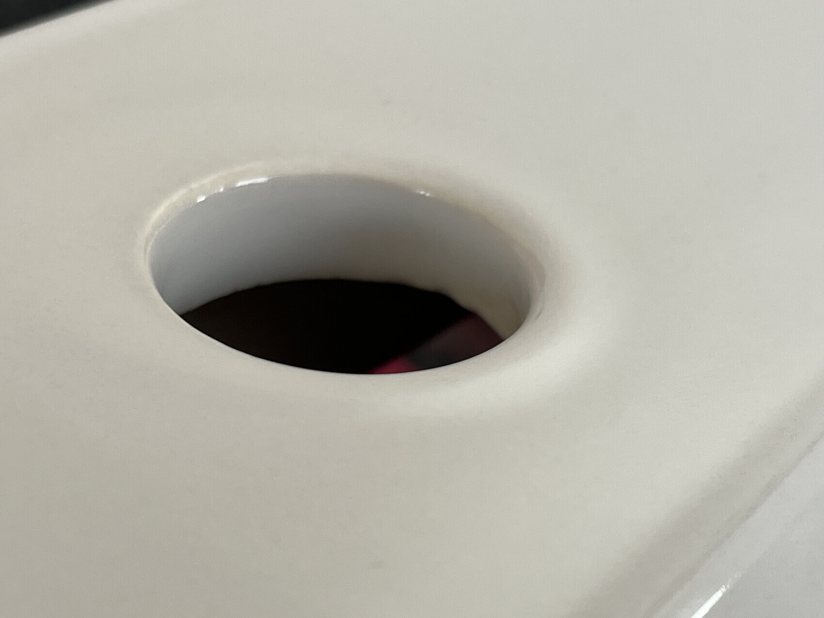 Runde Öffnung in einer weißen Oberfläche mit dunklem Innenraum, Blick ins Loch