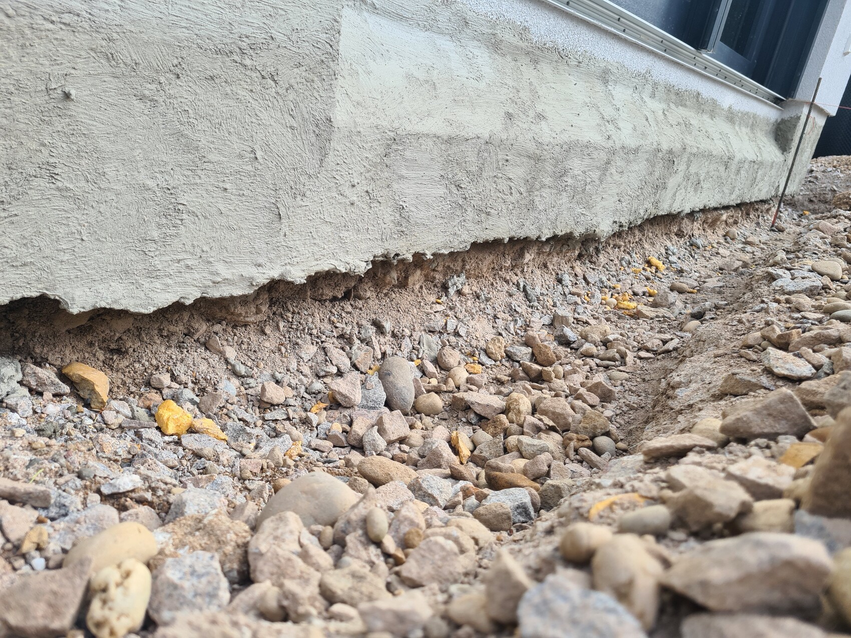 Unterkante eines Hauses mit freigelegtem Kies und Erdreich um die Fundamentwand