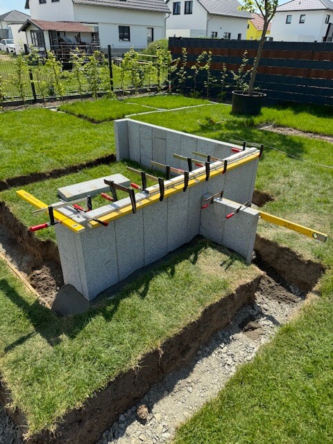 Gartenbaustelle: Betonfundamentwand im Graben, gelbe Wasserwaagen liegen auf der Wand.