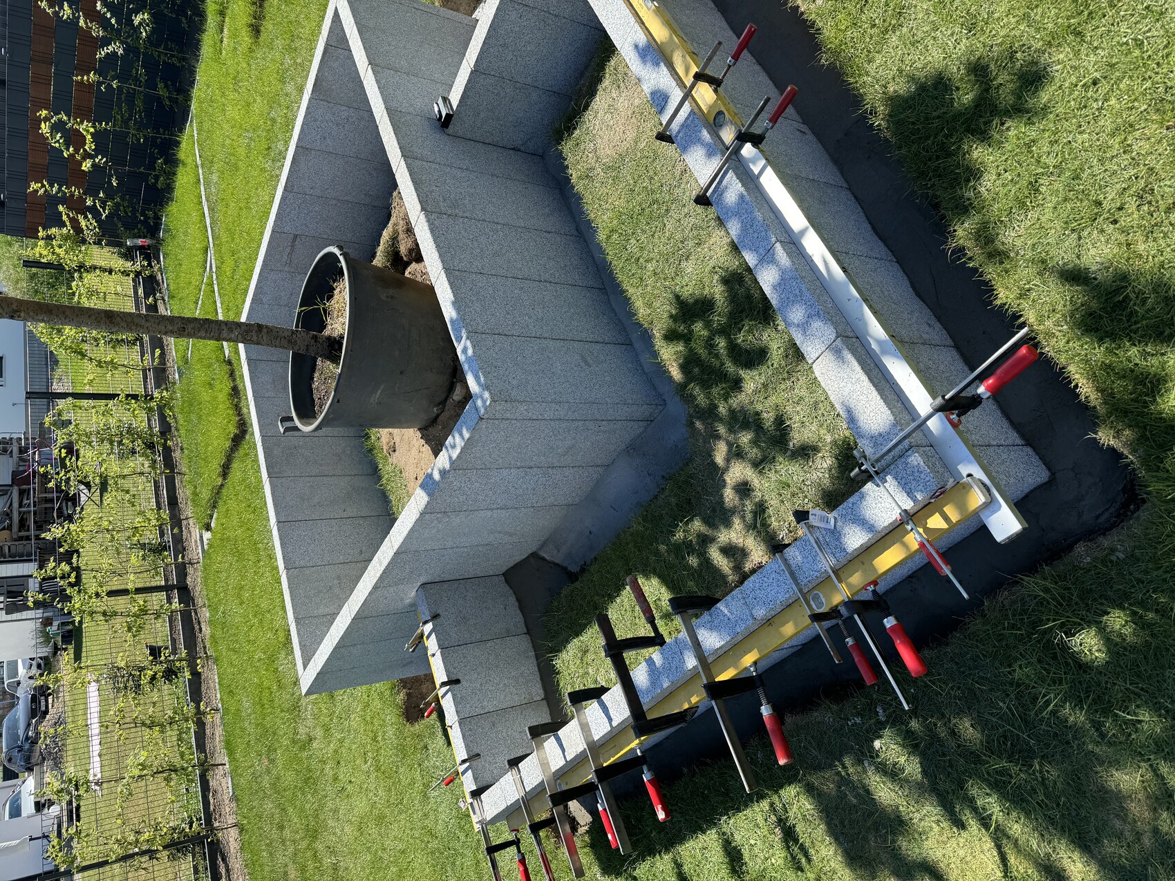 Garten: quadratische Betonblockmauer um Pflanzkübel mit Baum; Klemmen und Wasserwaage daneben.