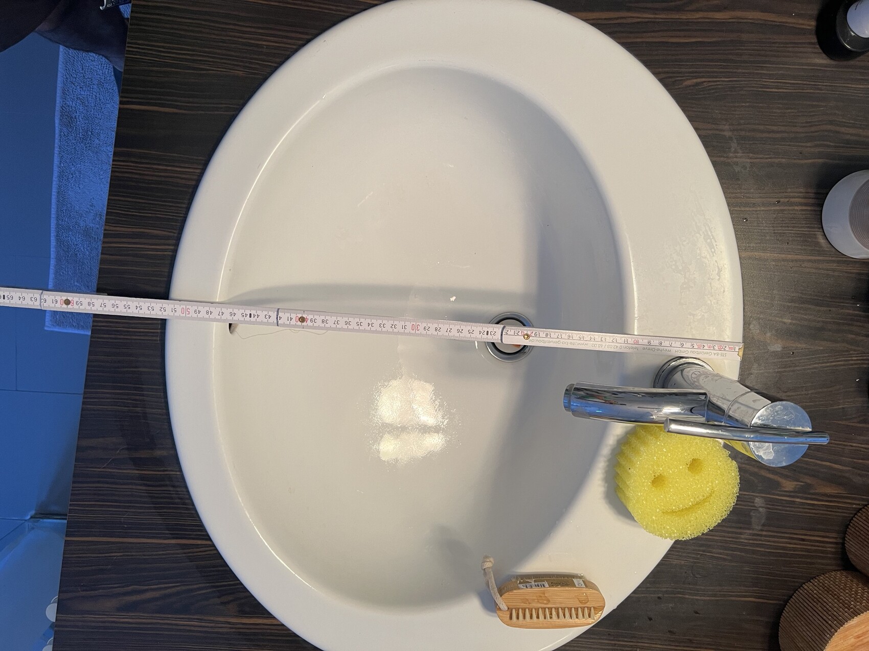 Weißes Waschbecken mit Messband quer darüber, gelber Smileyschwamm und Reinigungsbürste.