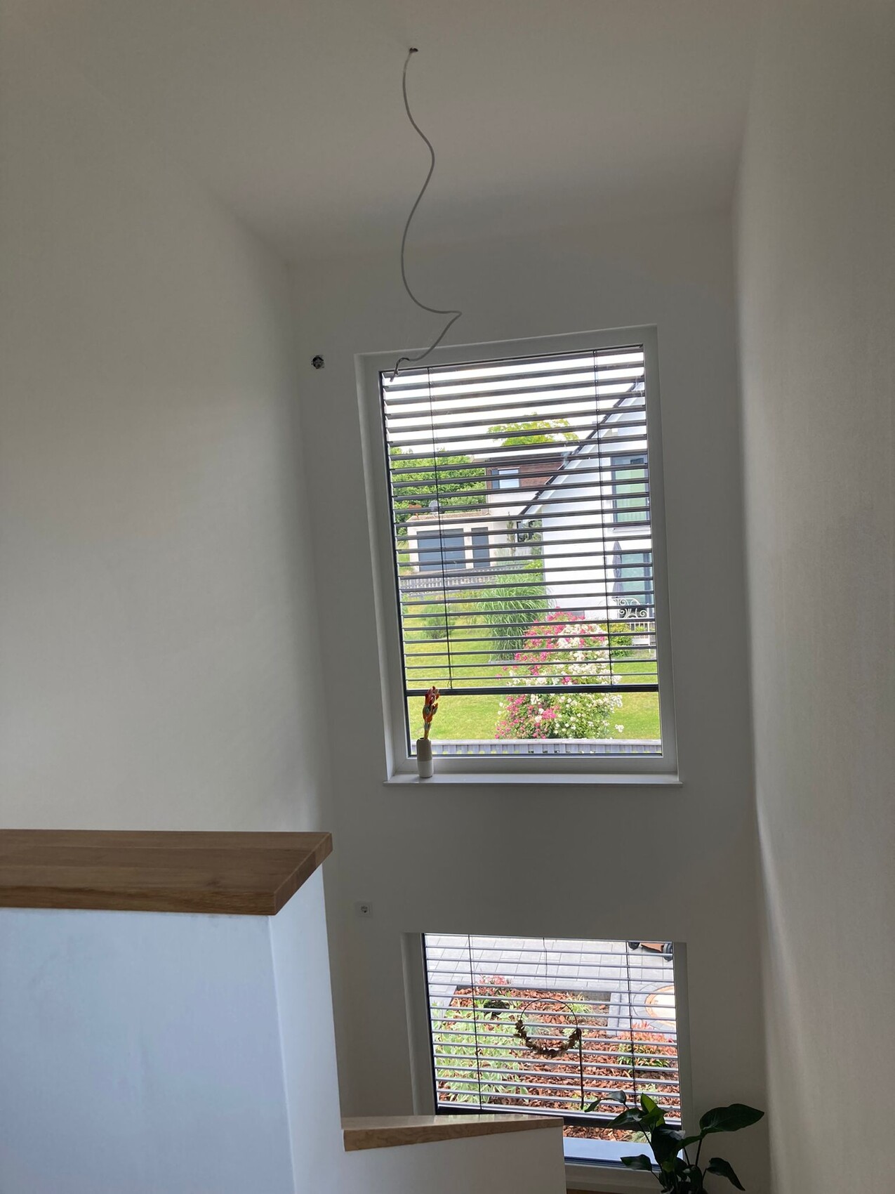 Helles Treppenhaus mit großen Fenstern, Vase am Fensterbrett, Garten zu sehen.