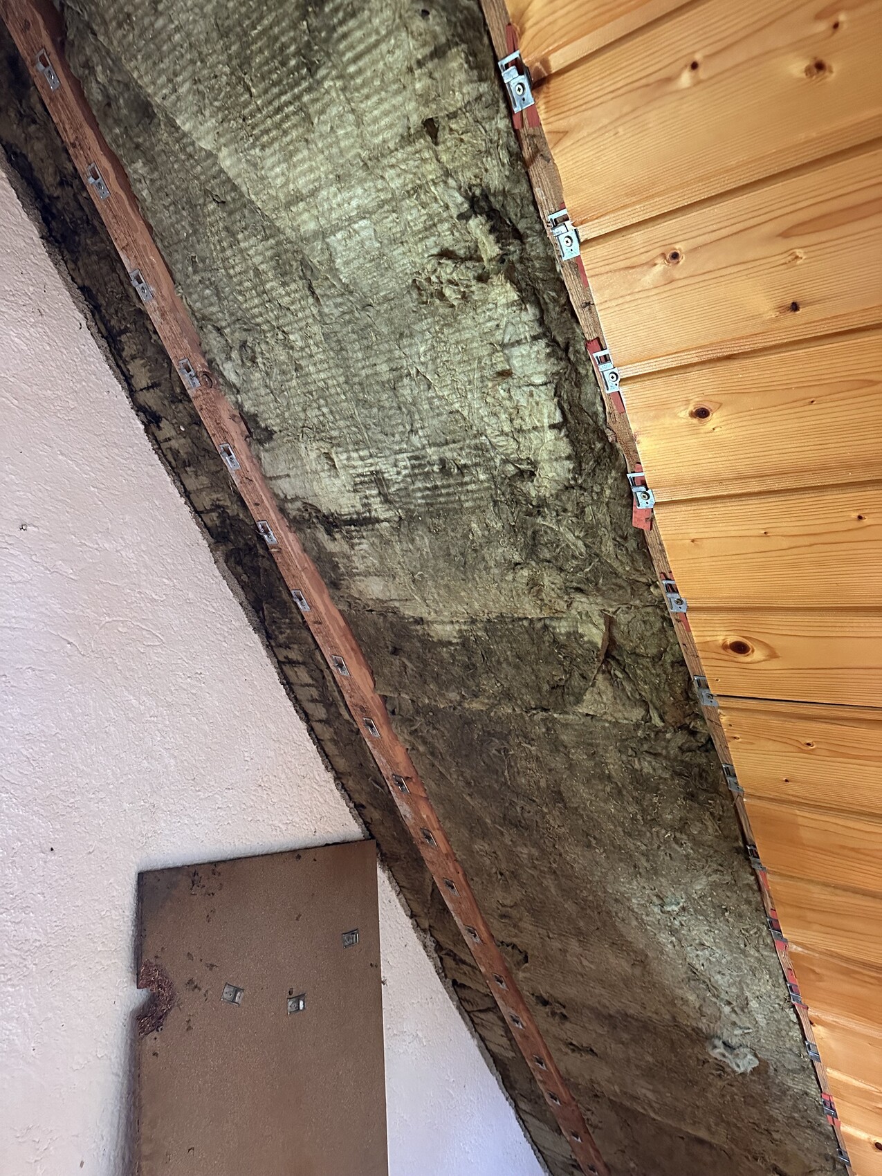Dachboden-Decke: Mineralwolle-Dämmung zwischen Holzlatten und Holzverkleidung, linke Wand verputzt.