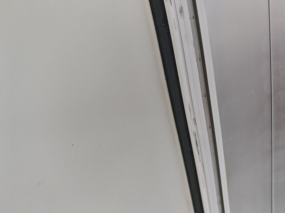 Nahaufnahme eines Tür- oder Fensterrahmens mit schwarzer Gummidichtung zwischen Metallflächen
