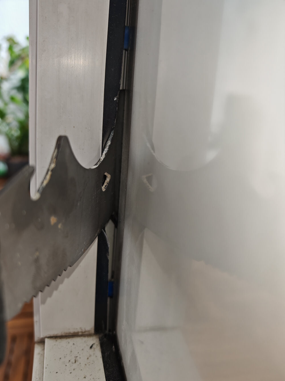 Nahaufnahme eines grobzahnigen Sägeblatts im Spalt zwischen weißem Rahmen und glatter Fläche.