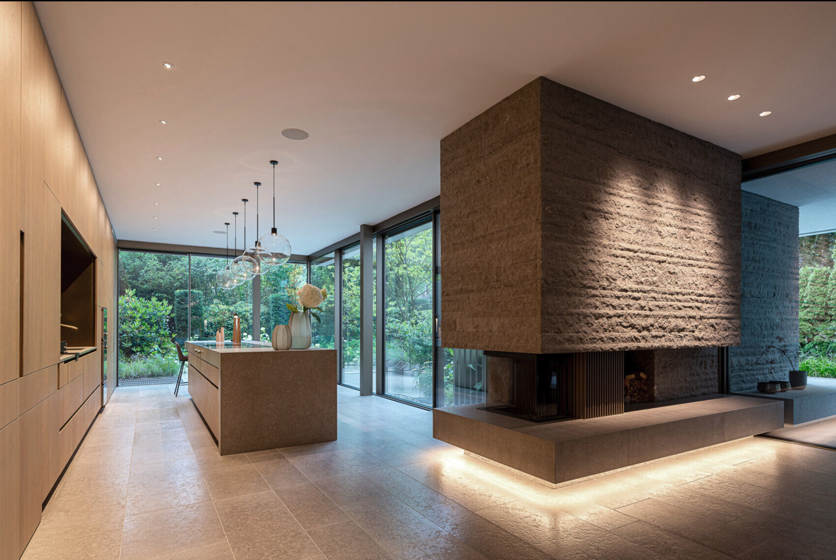 Moderne offene Küche mit großer Stein-Kaminstruktur, Insel und Blick auf den Garten.