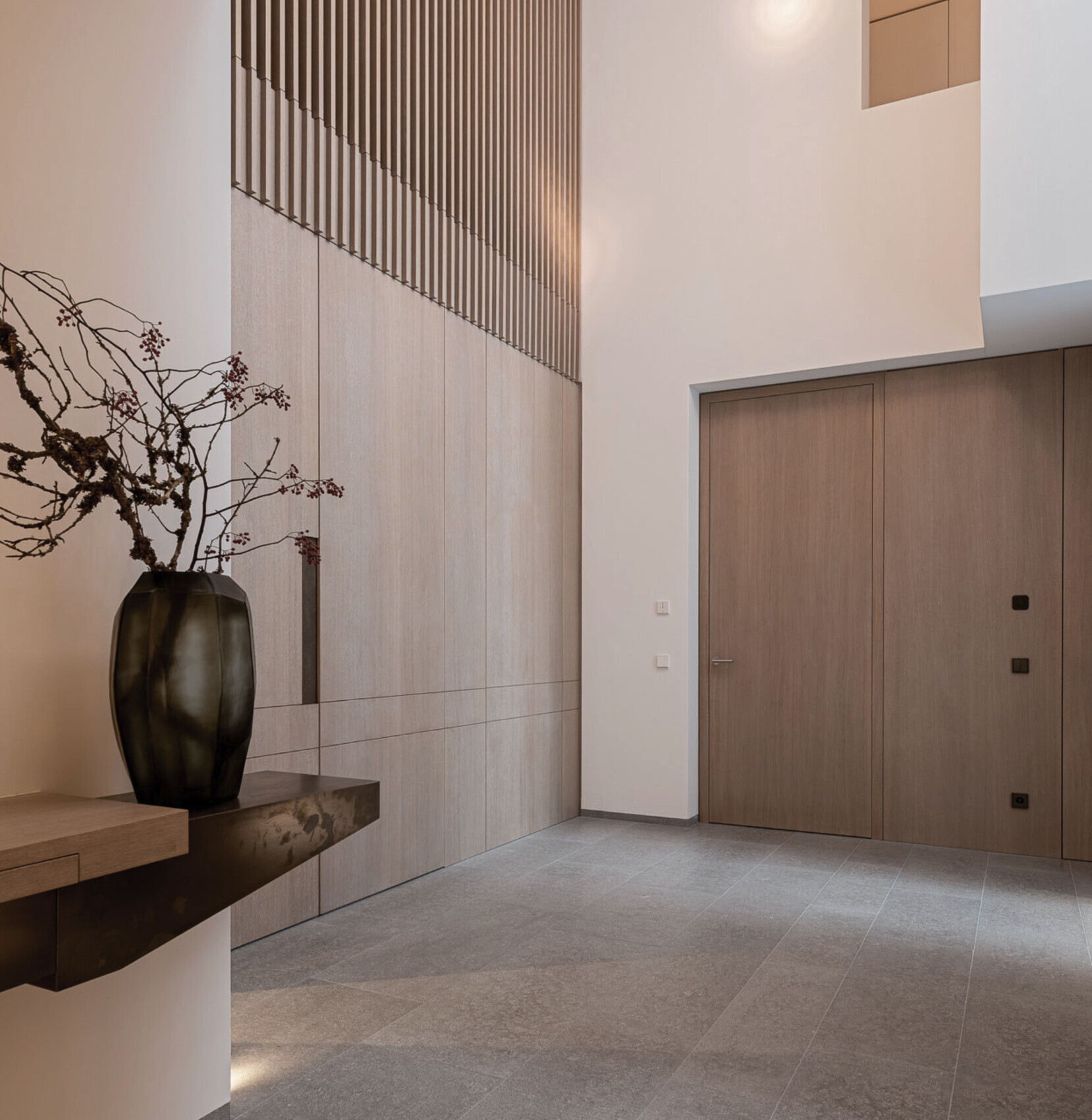 Moderner Eingangsbereich mit Holzverkleidung, großen Holztüren und Vase mit Zweigen.