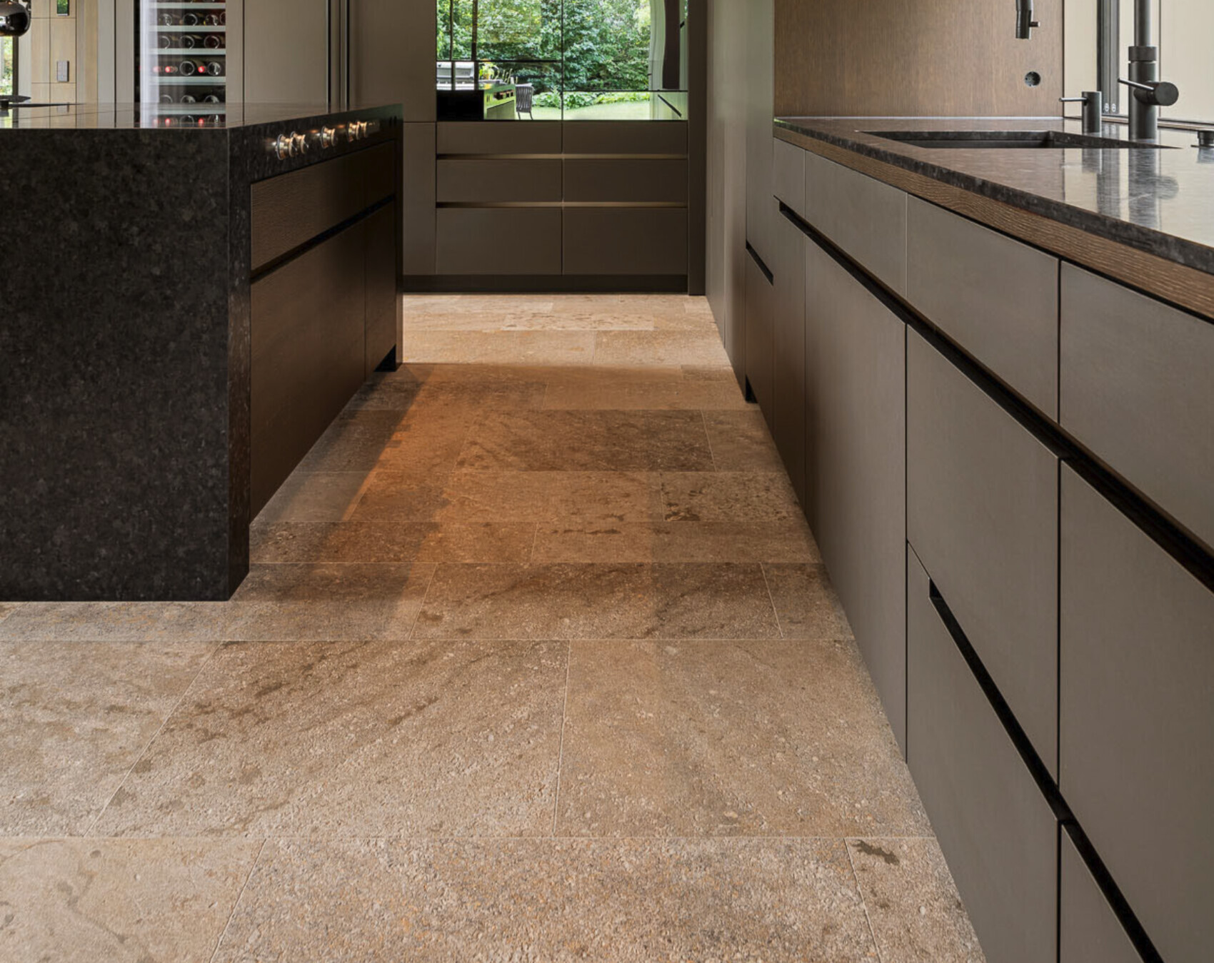 Moderne Küche mit Insel links, dunkler Steinplatte, graue Schränke, Spüle rechts, Blick nach Garten.