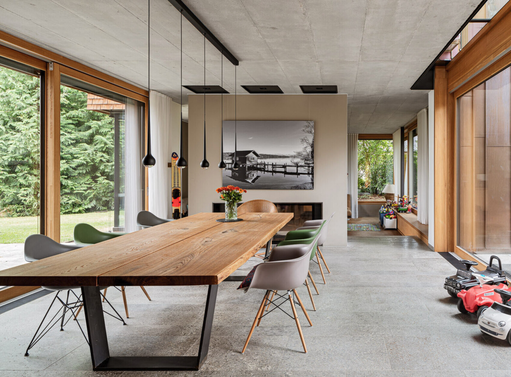 Helles Esszimmer mit langem Holztisch, schwarzen Hängelampen, Kamin und Schwarzweiß-Bild.