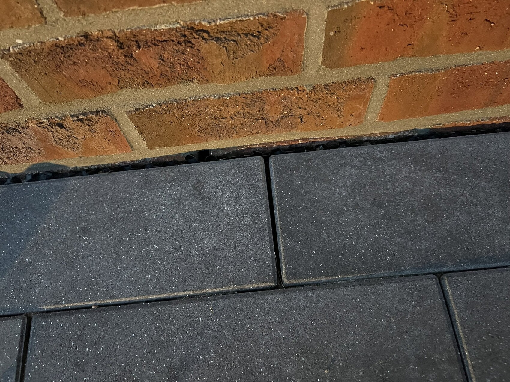 Ziegelwand über dunklen Pflastersteinen; schmale Fuge trennt zwei benachbarte Platten.