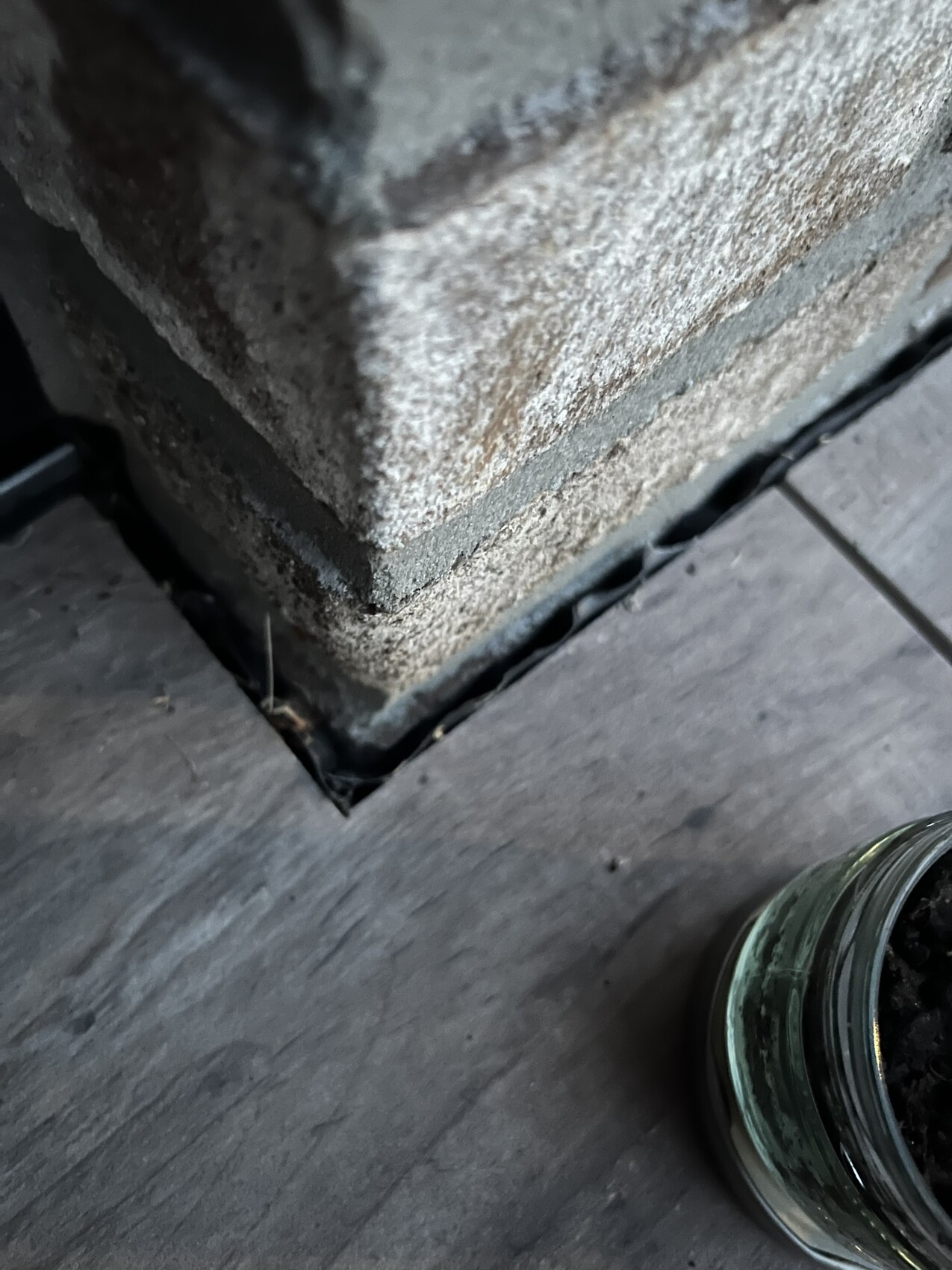 Nahaufnahme eines Ziegelpfostens auf einer Holzdiele; Glasgefäß mit Erde daneben.