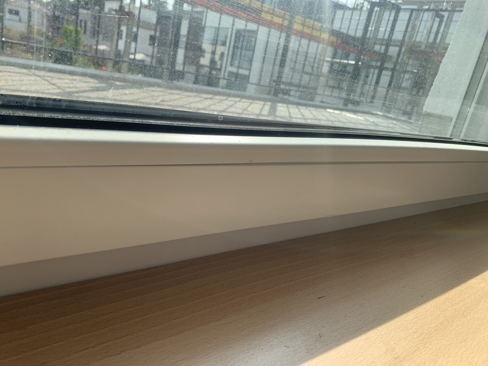 Blick durch ein Fenster auf eine Glasfassade draußen; innen weiße Fensterbank und Holztisch.