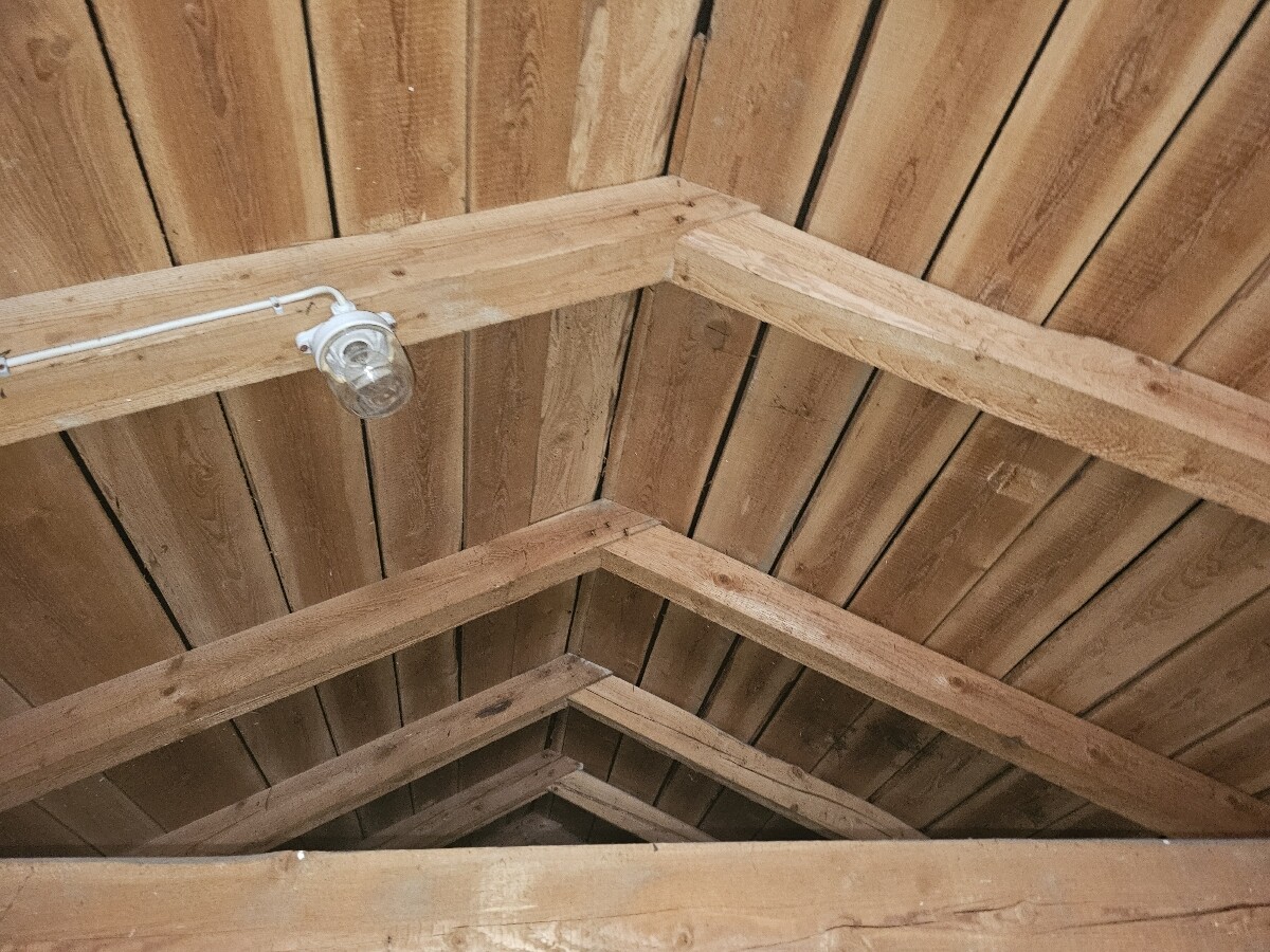 Dachboden mit offenem Holz-Dachstuhl und einer Glühbirne an einer Leitung.