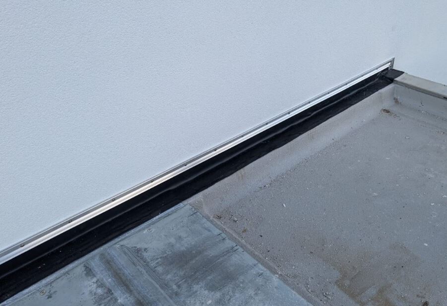 Flachdachkante mit schwarzer Dachabdichtung und Metallprofil an weißer Außenwand