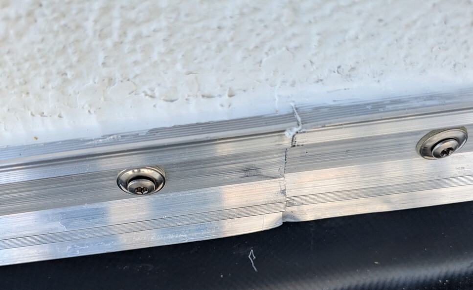 Aluminium-Türschwelle mit Schraubköpfe, sichtbare Fuge, weiße strukturierte Wand darüber.