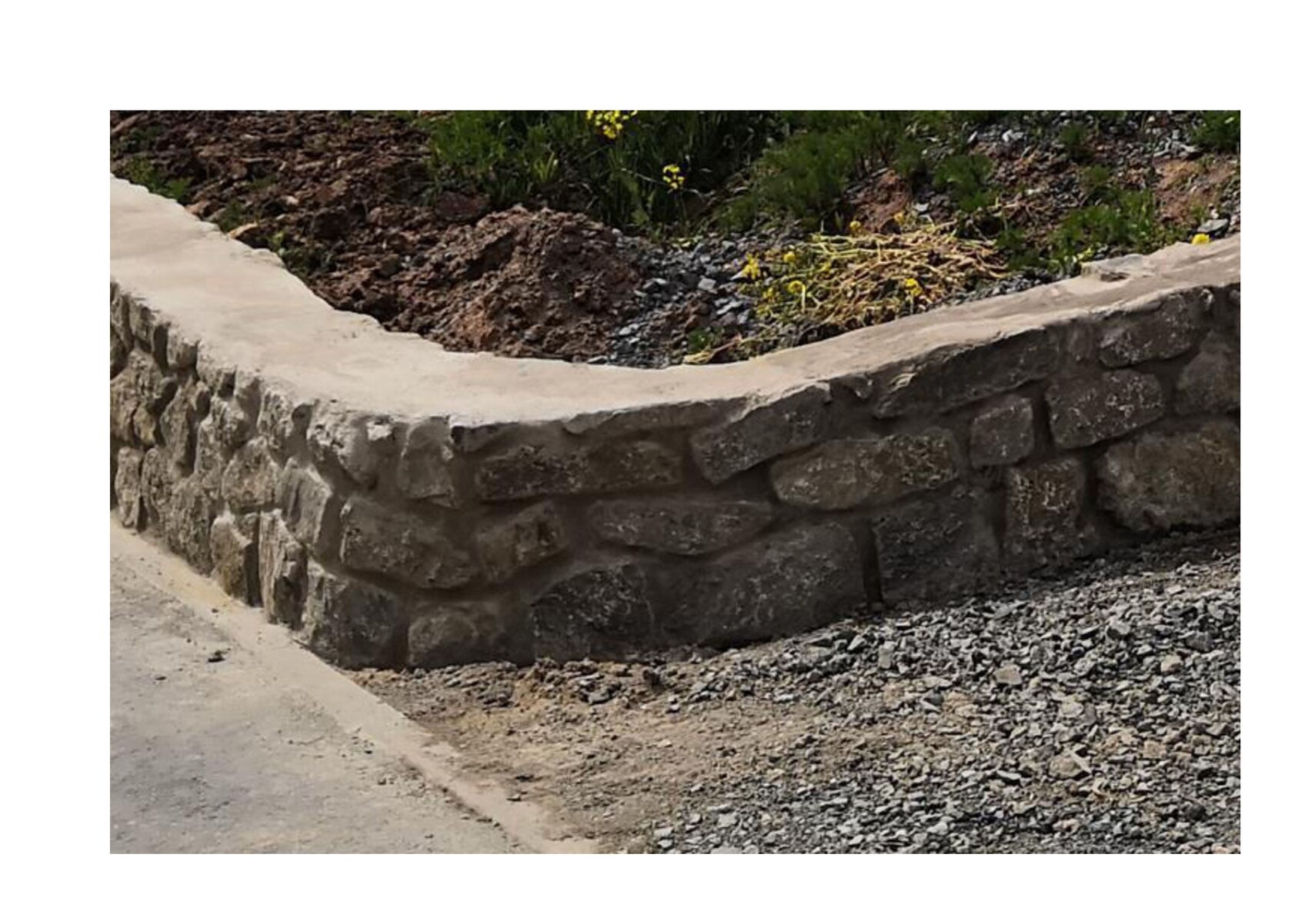 Grobe Natursteinmauer als Stützwand neben Kiesweg; Erdreich mit Pflanzen darüber.