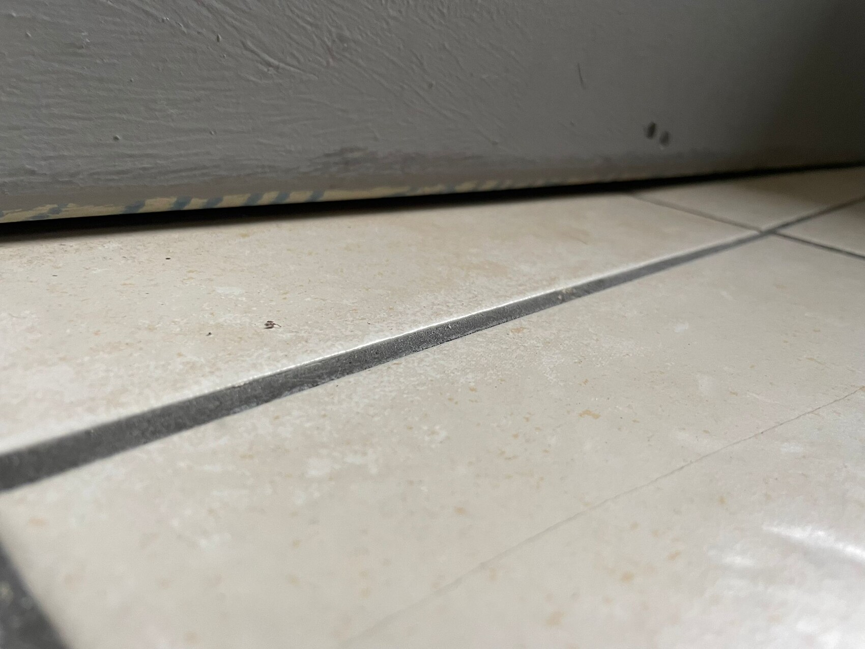 Nahaufnahme von Bodenfliesen mit Fugen und grauer Möbelkante am oberen Rand
