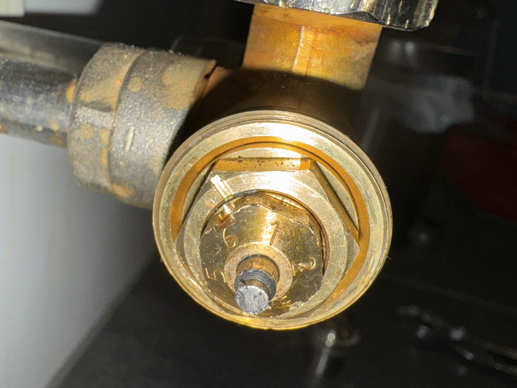 Nahaufnahme eines verrosteten Messingbauteils mit orangefarbener Dichtung und zentraler Schraubachse.